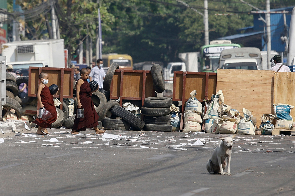 Dua biksu muda berjalan di depan barikade yang dibuat pengunjuk rasa di kota Yangon, Myanmar, Kamis (11/3)  