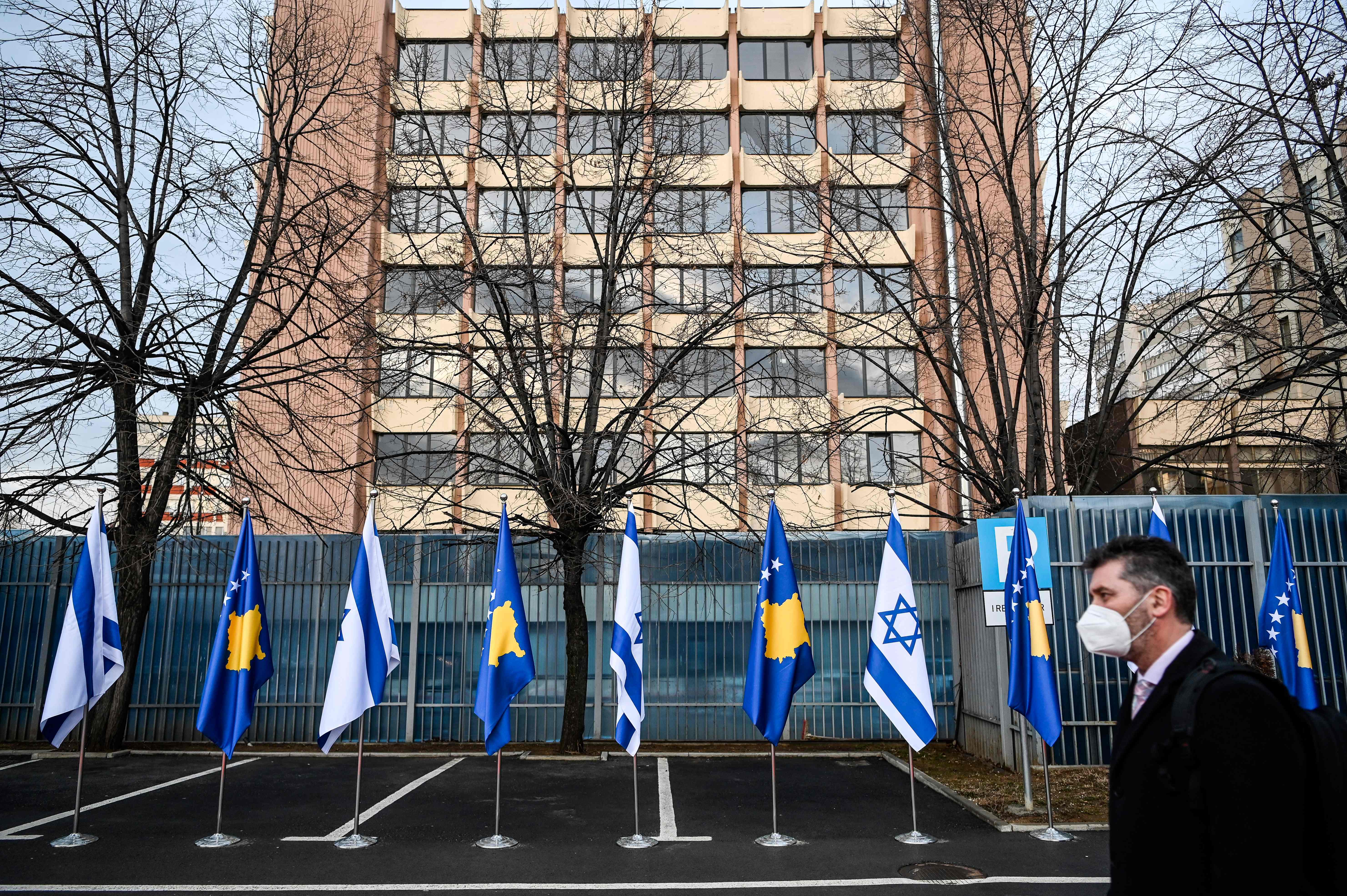 Seorang warga melintas di depan rangkaian bendera Kosovo dan Israel di Pristina, Kosovo.