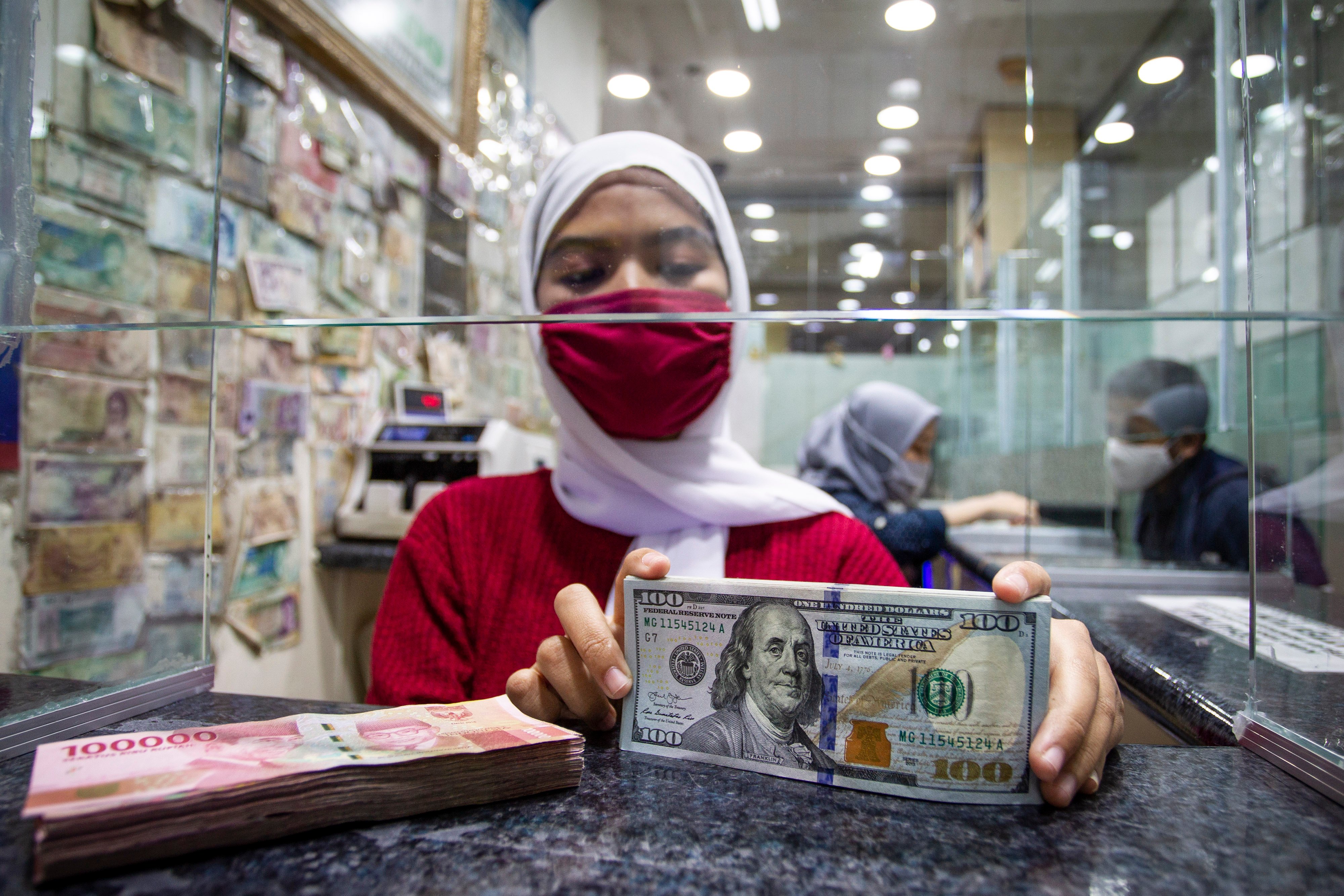 Petuga menujukkan mata uang dolar AS yang akan ditukarkan ke Rupiah