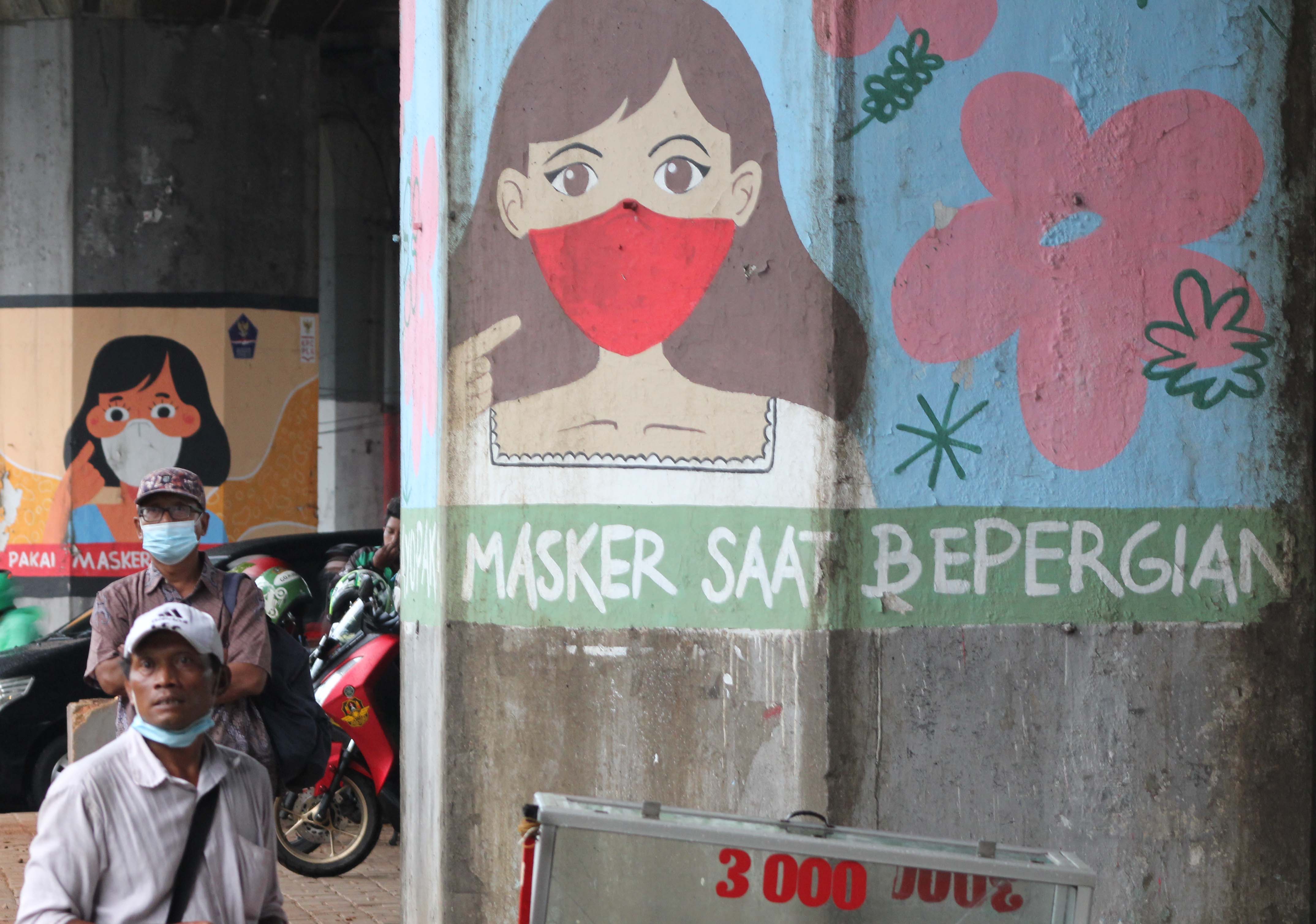 Warga melintasi mural terkait sosialisasi prokes di wilayah Jakarta.