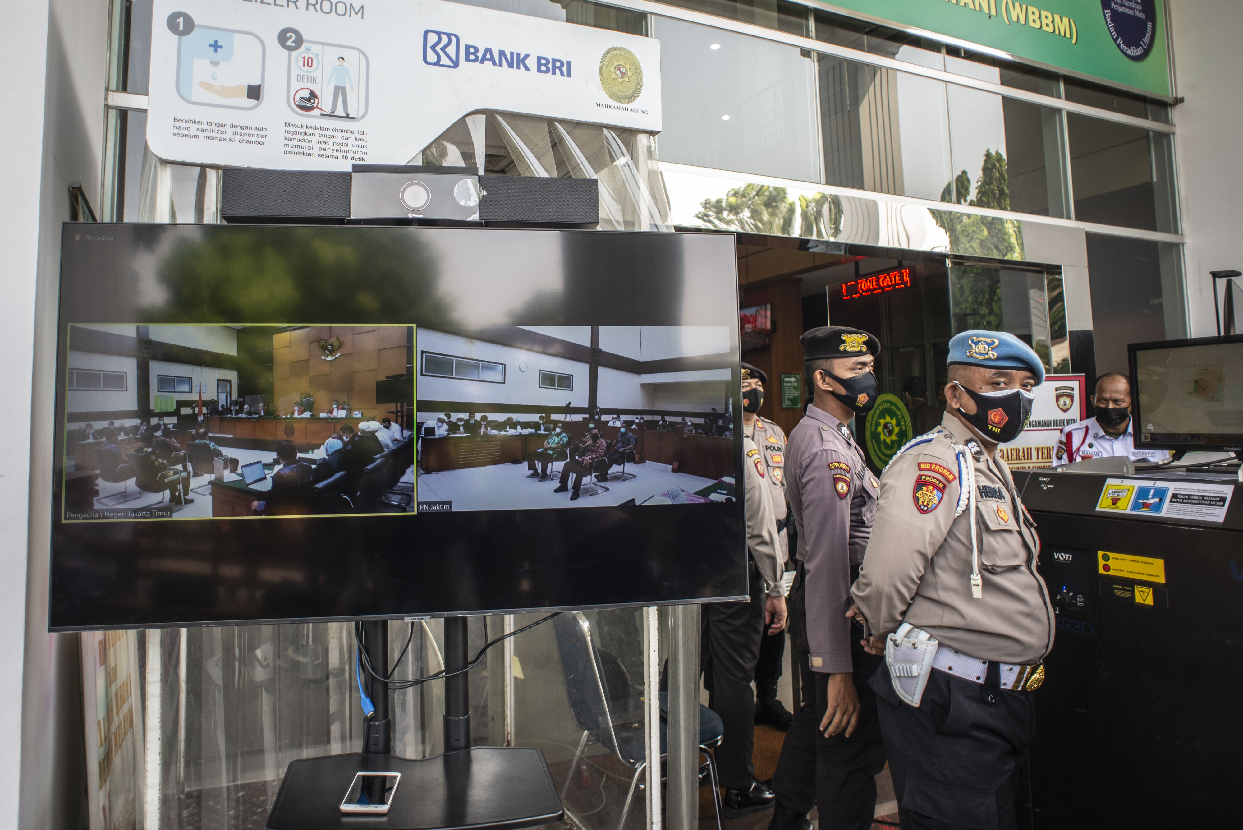 Polisi berada di dekat layar yang menampilkan suasana sidang kasus pelanggaran prokes dengan terdakwa Rizieq Shihab di PN Jakarta Timur.