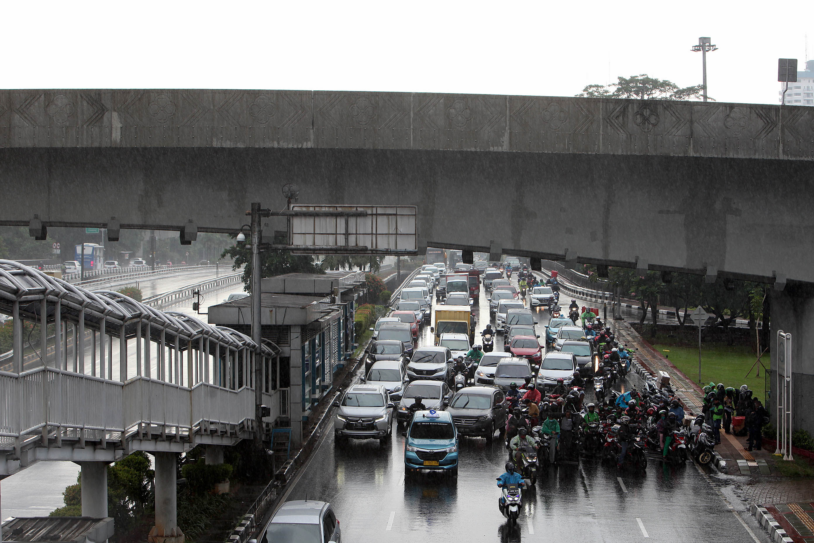 Pengendara sepeda motor berteduh di bawah jembatan saat hujan di Jakarta