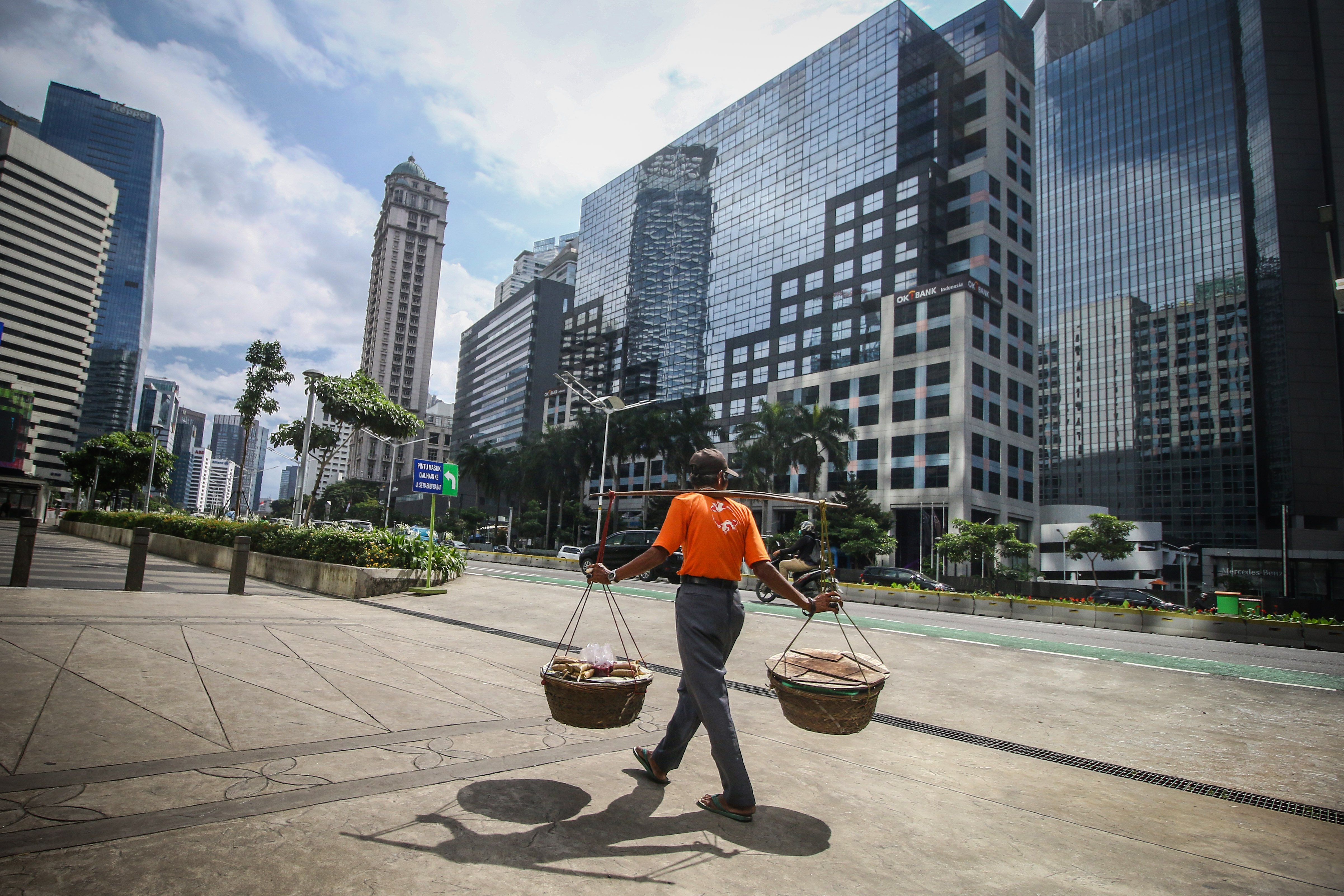 Pedagang melintasi kawasan gedung bertingkat di Jalan Jenderal Sudirman, Jakarta.