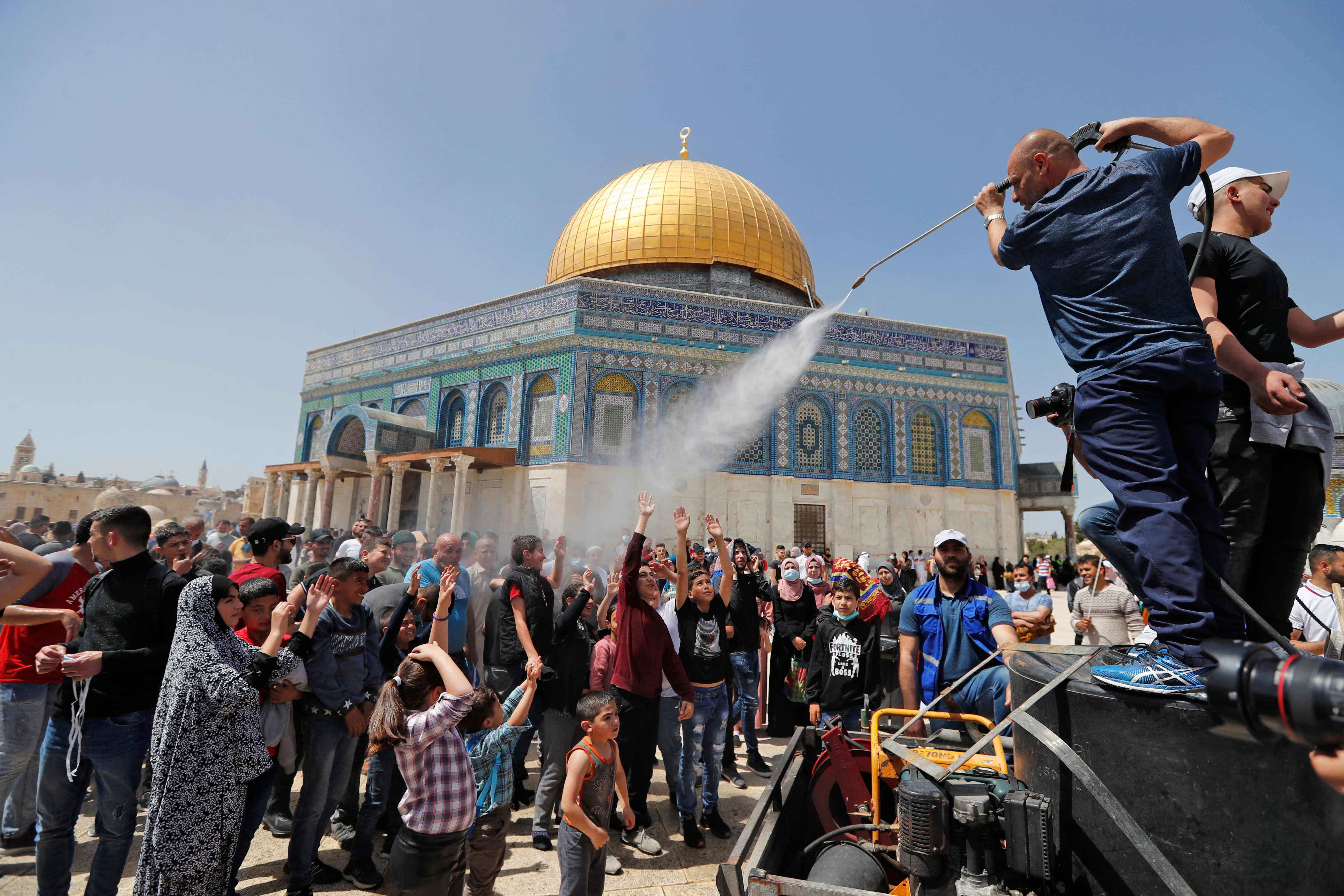 Seorang pria menyemprot orang Palestina dengan air untuk mendinginkan mereka saat berkumpul untuk mengambil bagian dalam salat Jumat.