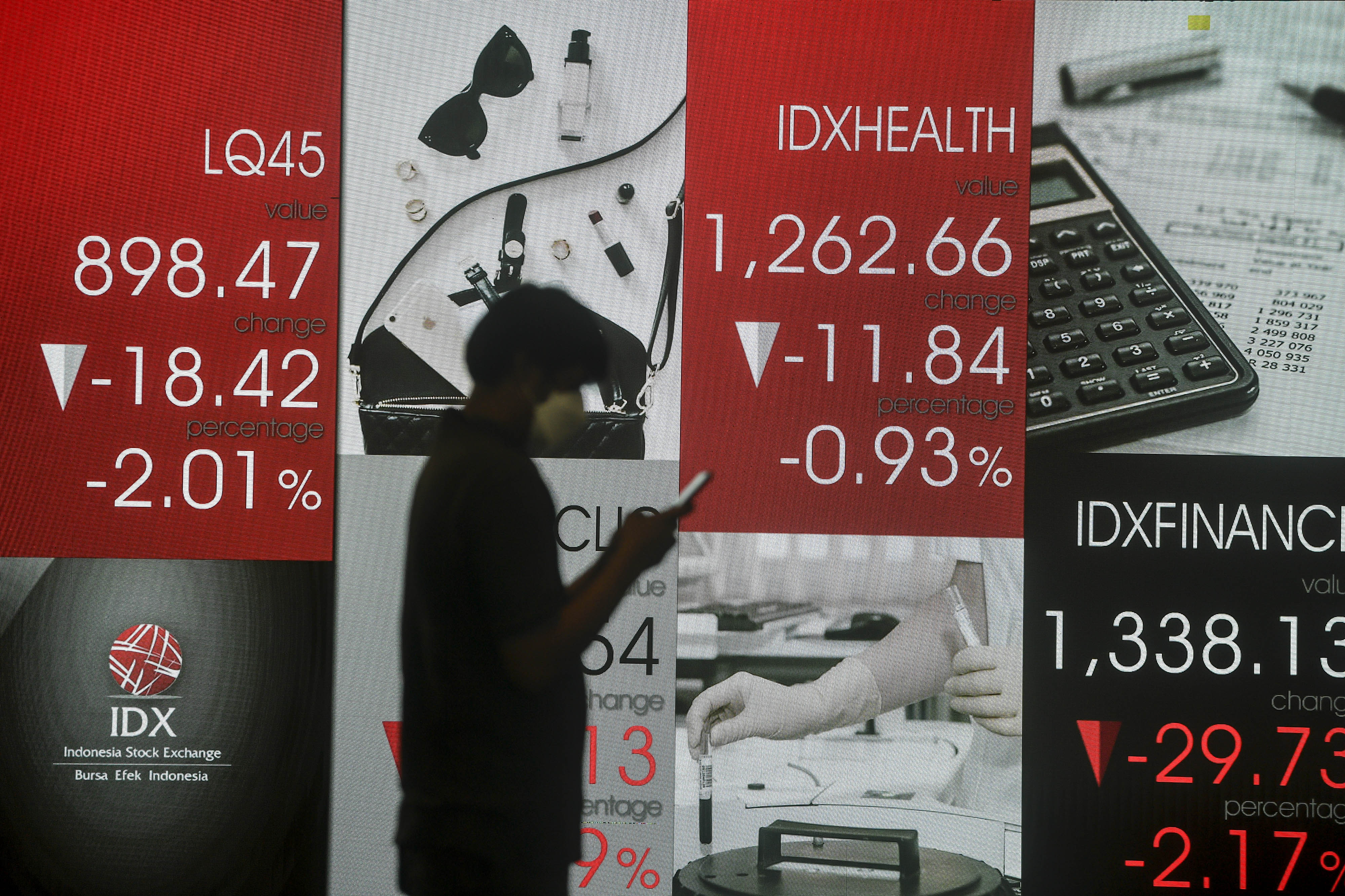 Pekerja melihat telepon pintarnya dengan latar belakang layar pergerakan harga saham di Bursa Efek Indonesia, Jakarta, Rabu (31/3/2021)