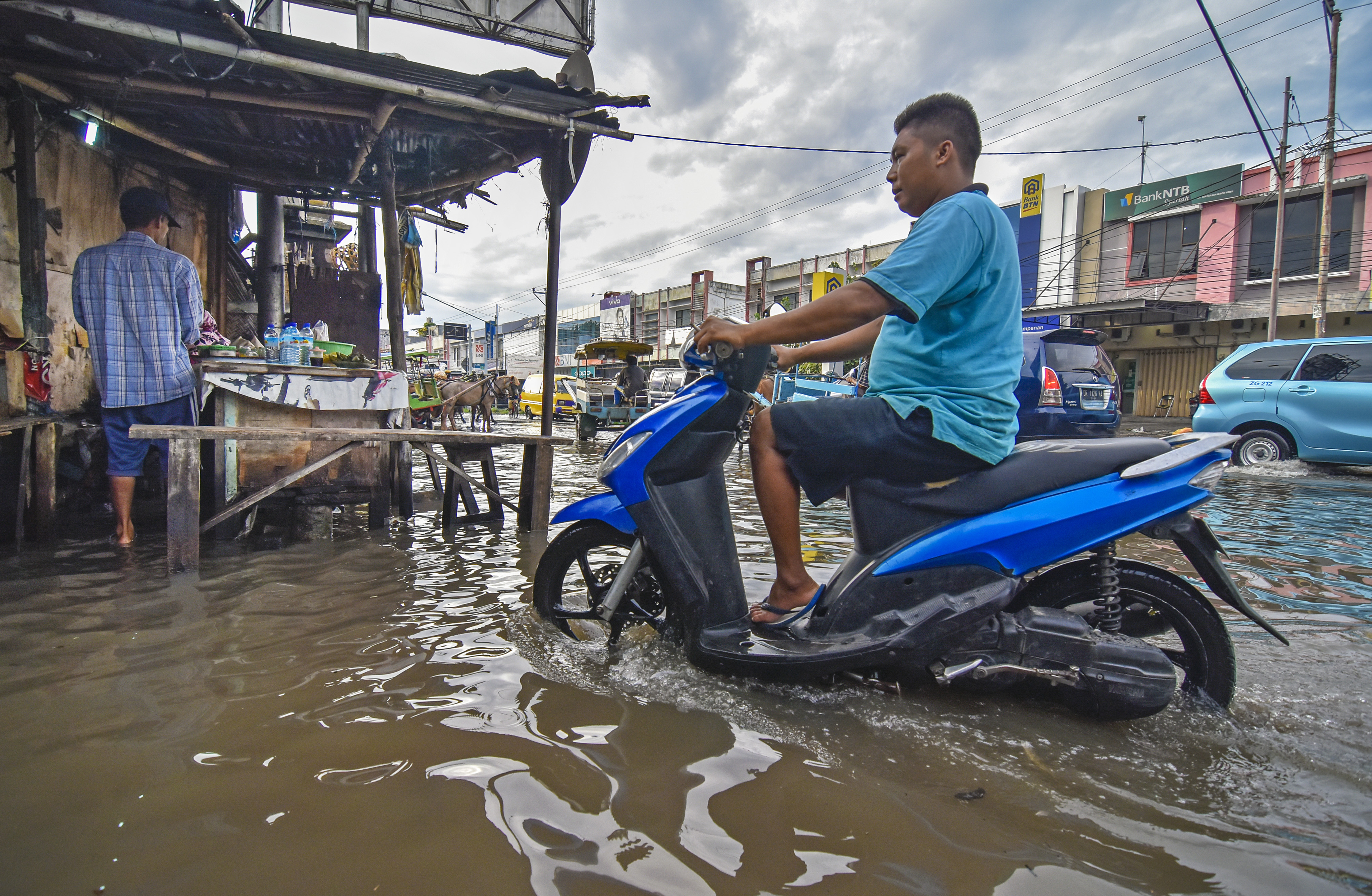  Seorang laki-laki menggunakan sepeda motor melintasi genangan air di jalan Pasar Kebon Roek, Ampenan, Mataram, NTB, Jumat (29/5/2020)