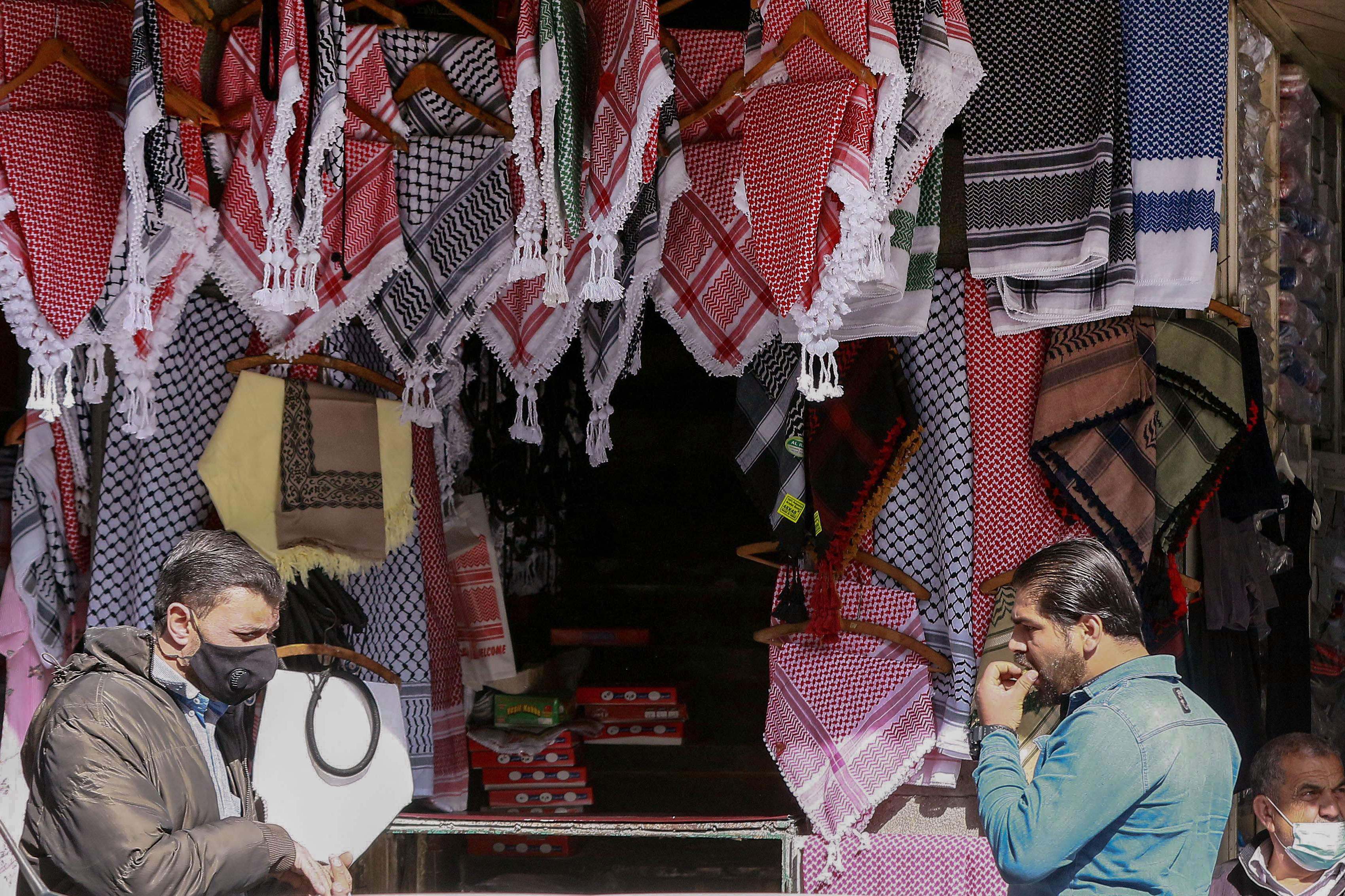 Orang-orang berjalan melewati toko yang menjual syal tradisional keffiyeh di jalan perbelanjaan ibu kota Amman, Yordania, Senin (5/4).