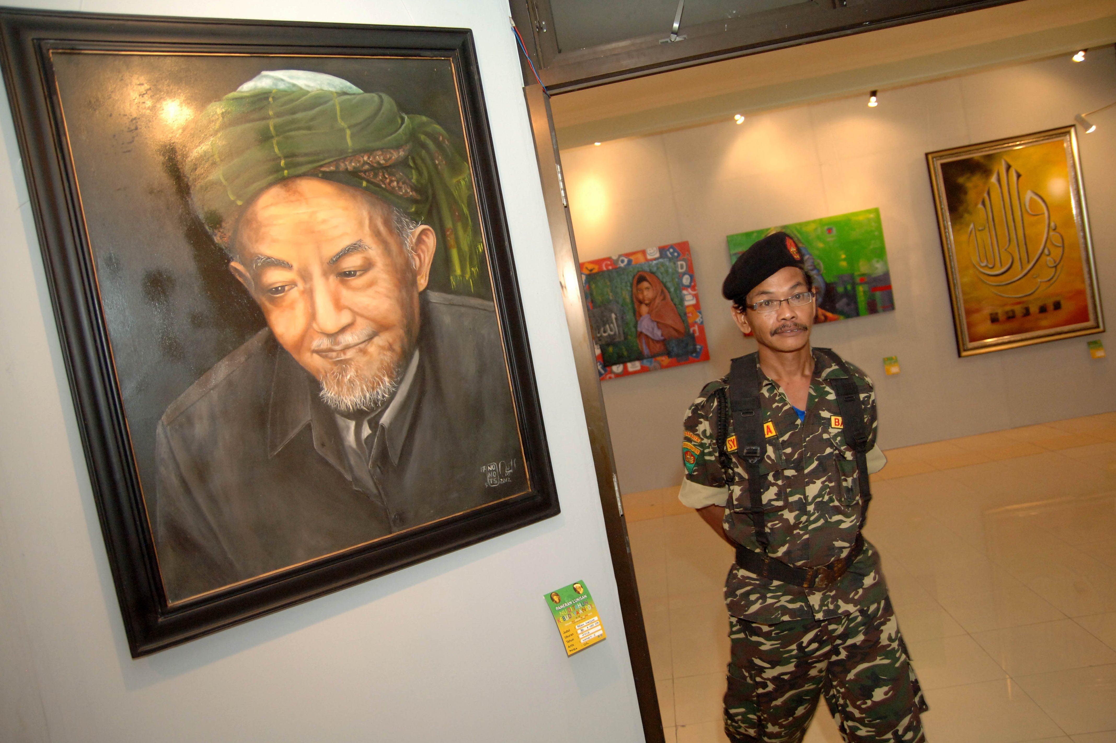 Seorang banser melintas disamping karya seni lukis bergambar KH Hasyim Asy'ari disela-sela festival seni di Kantor PWNU Jatim, Surabaya.