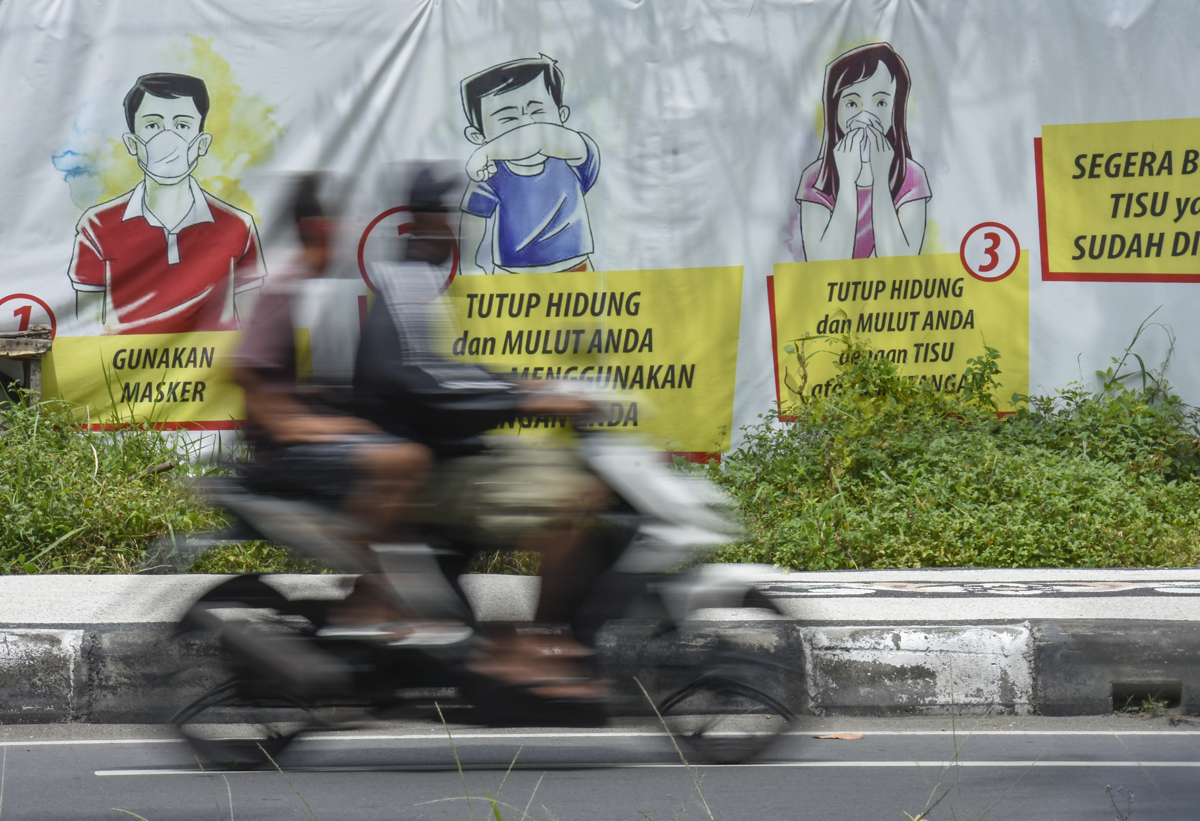 Pengendara sepeda motor melintas dekat poster sosialisasi pencegahan COVID-19 di Jalan Udayana, Mataram, NTB, Senin (22/3/2021)-ilustrasu