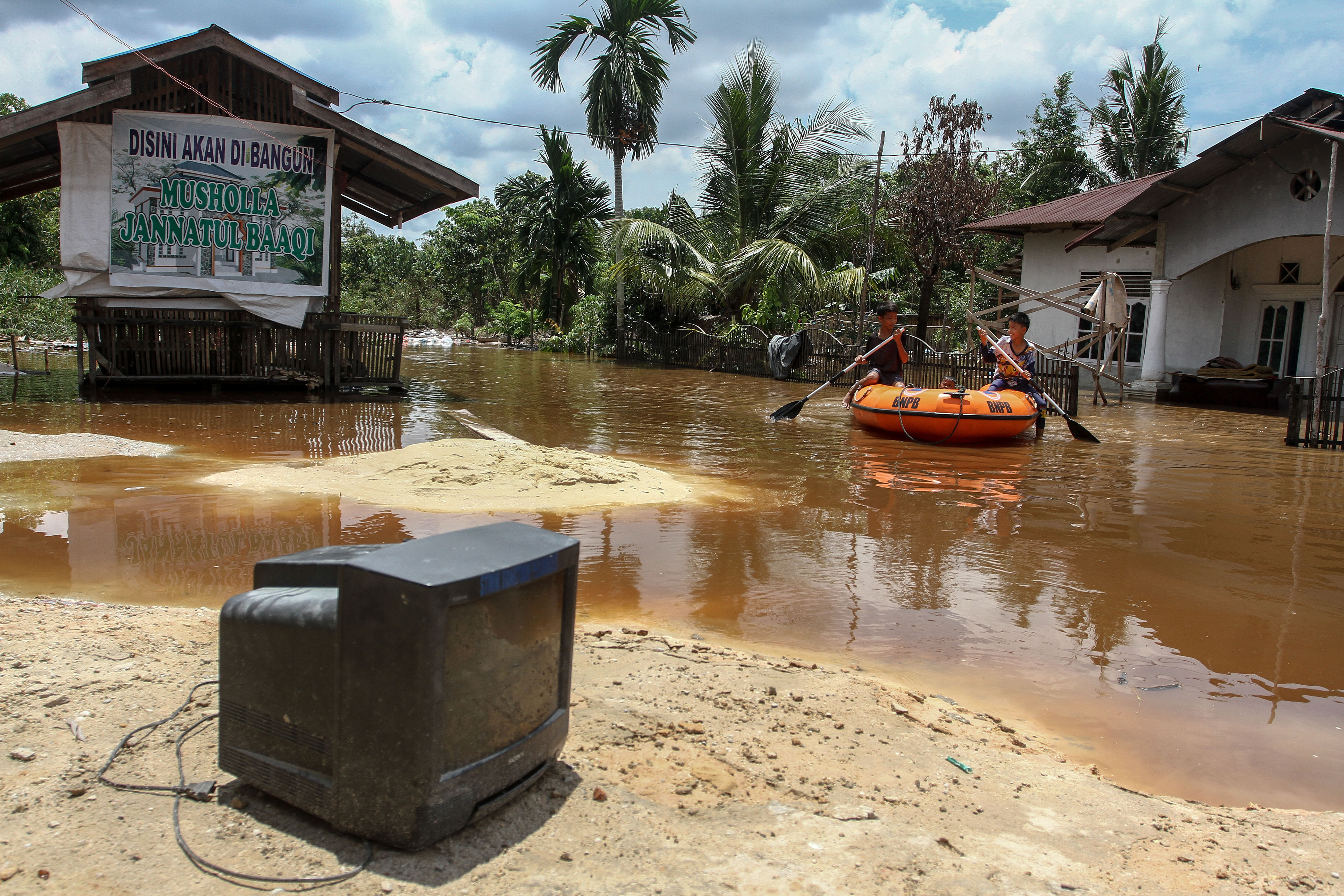 Sejumlah anak bermain perahu karet di depan rumah yang terendam banjir akibat luapan Sungai Sail di Pekanbaru, Riau, Jumat (23/4/2021)