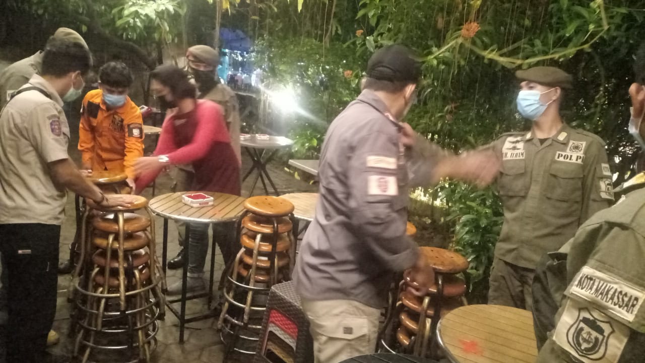 Satpol PP Kota Makassar mengangkut kursi-kursi di tempat makan yang melakukan pelanggaran protokol kesehatan. 