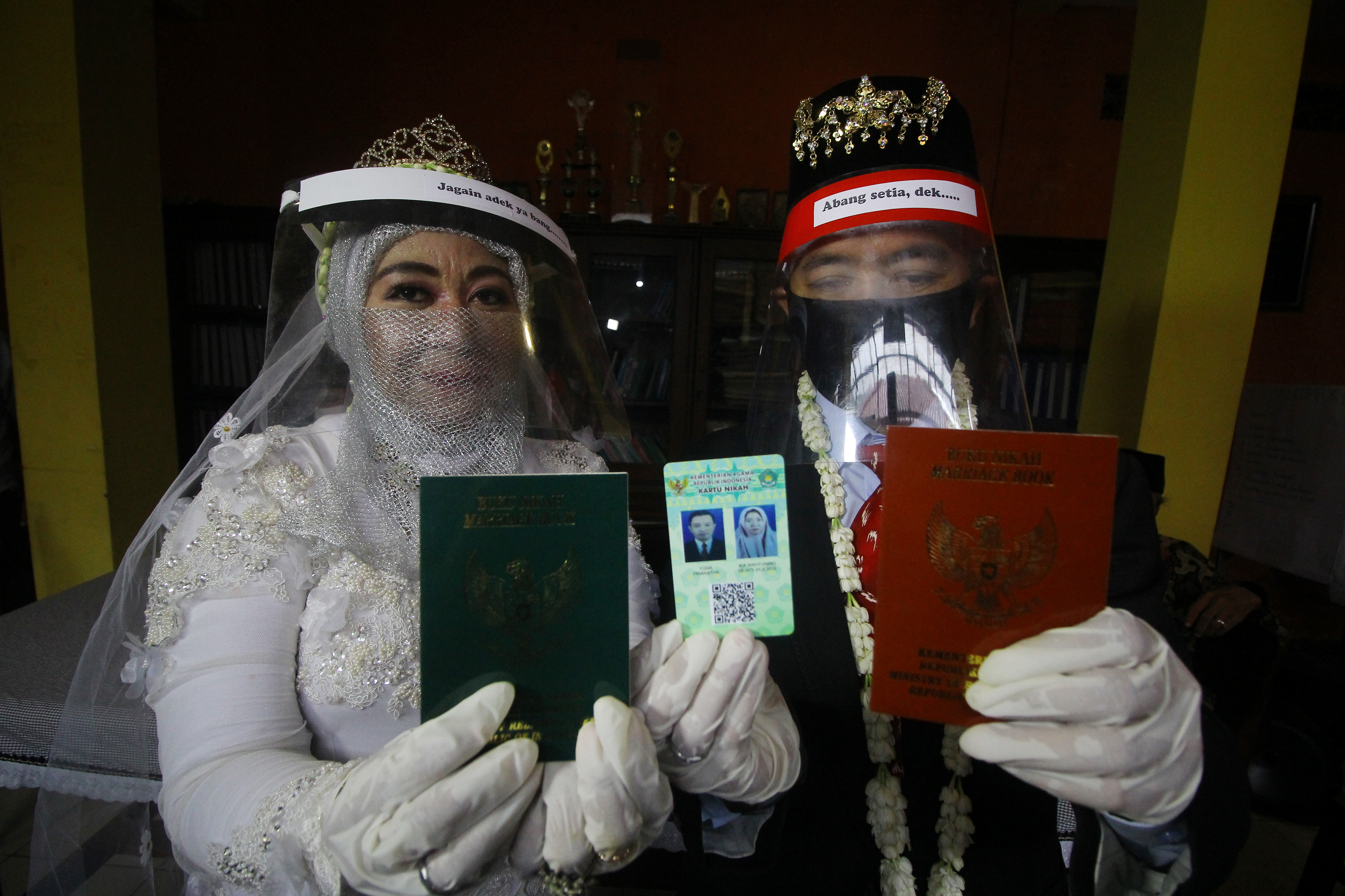 Pasangan pengantin memperlihatkan buku dan kartu nikah usai melaksanakan akad nikah di KUA Tandes, Surabaya, Jawa Timur, Kamis (21/5).