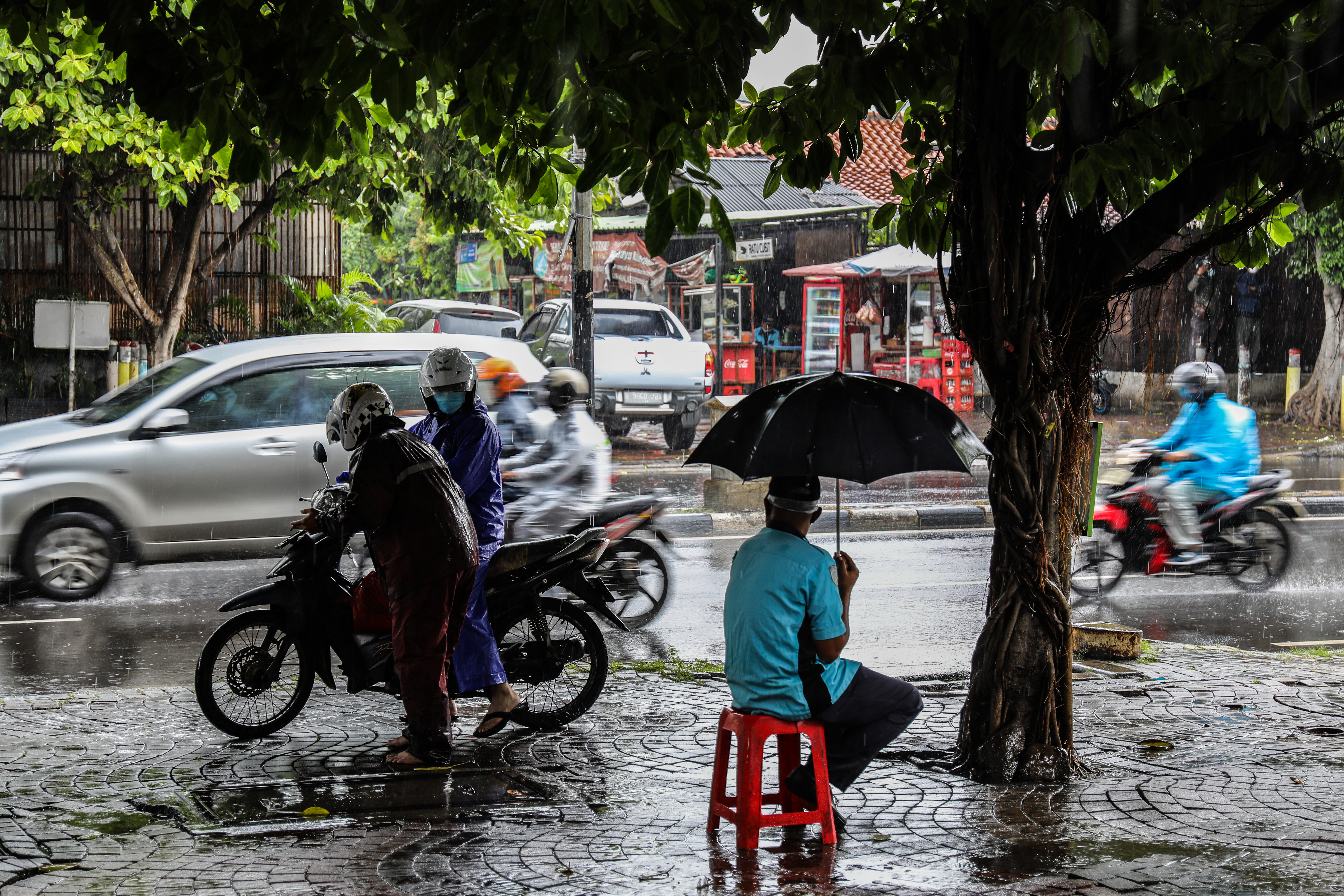 Petugas parkir mengenakan payung untuk menahan hujan di trotoar kawasan Menteng Jakarta Pusat.