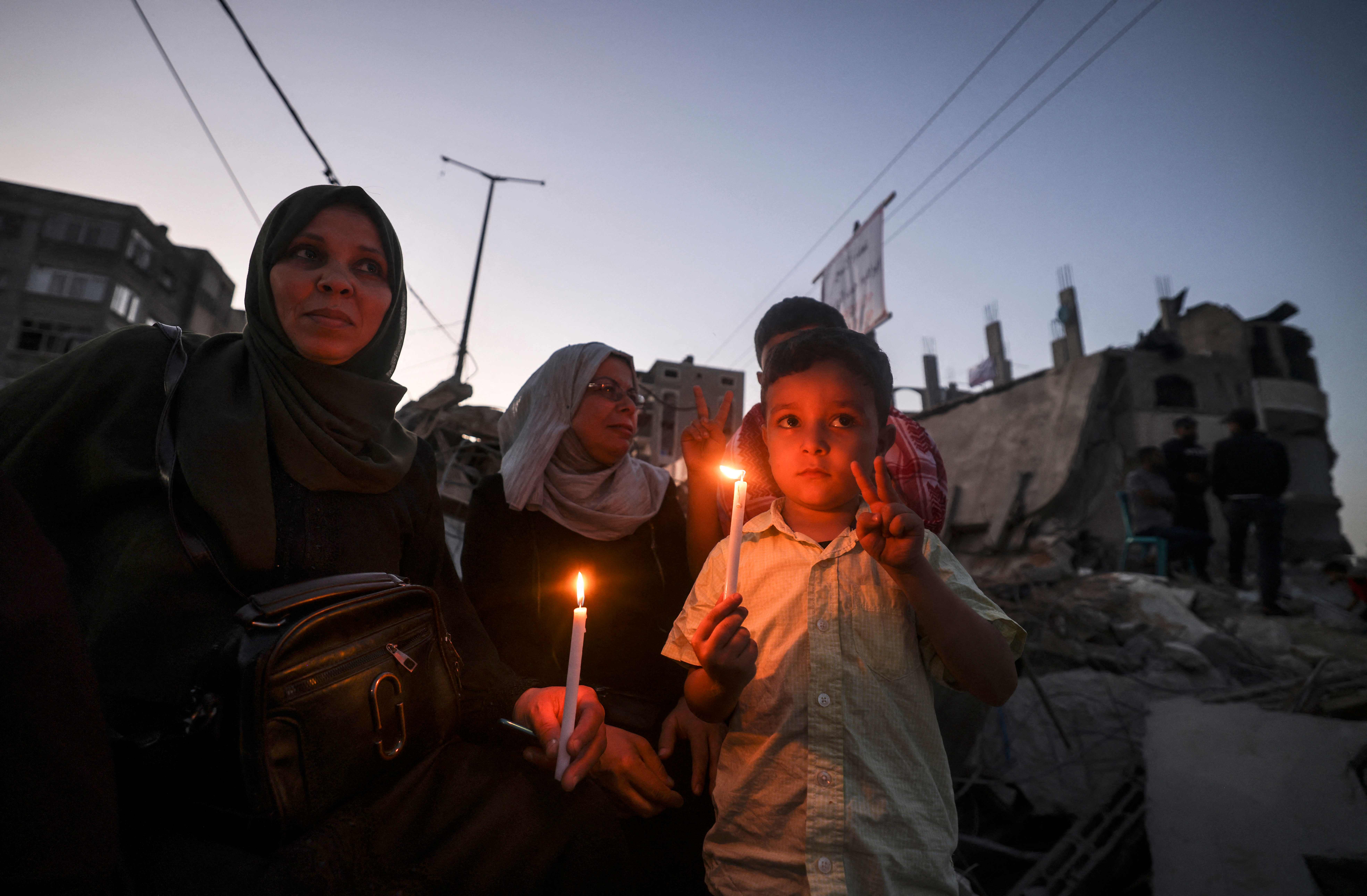 Warga Palestina membawa lilin saat mengunjungi rumah mereka yang hancur akibat serangan udara Israel di Jalur Gaza.