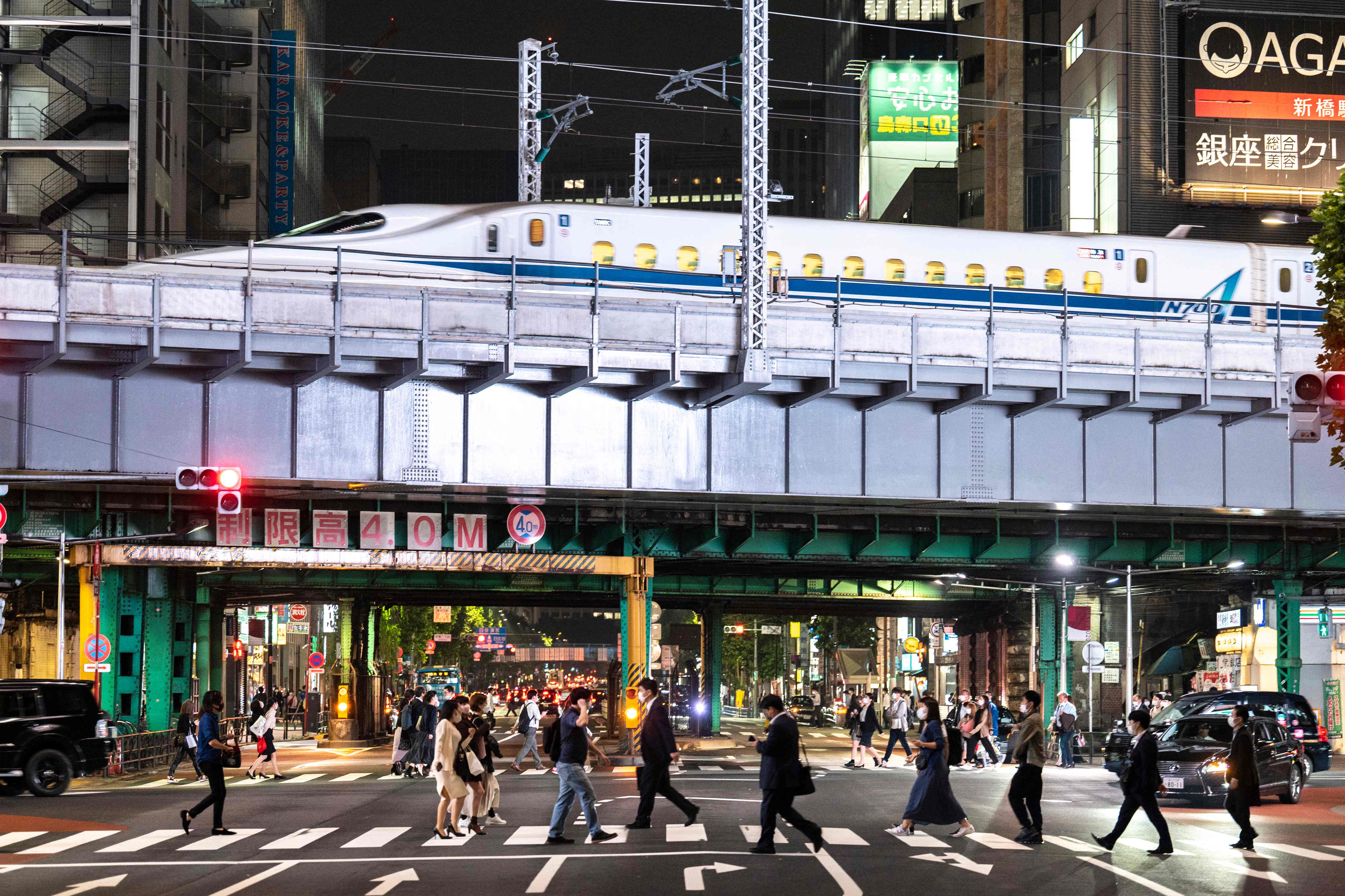 Warga menyeberang jalan saat Shinkansen melintas di dekat mereka di Tokyo, Jepang.