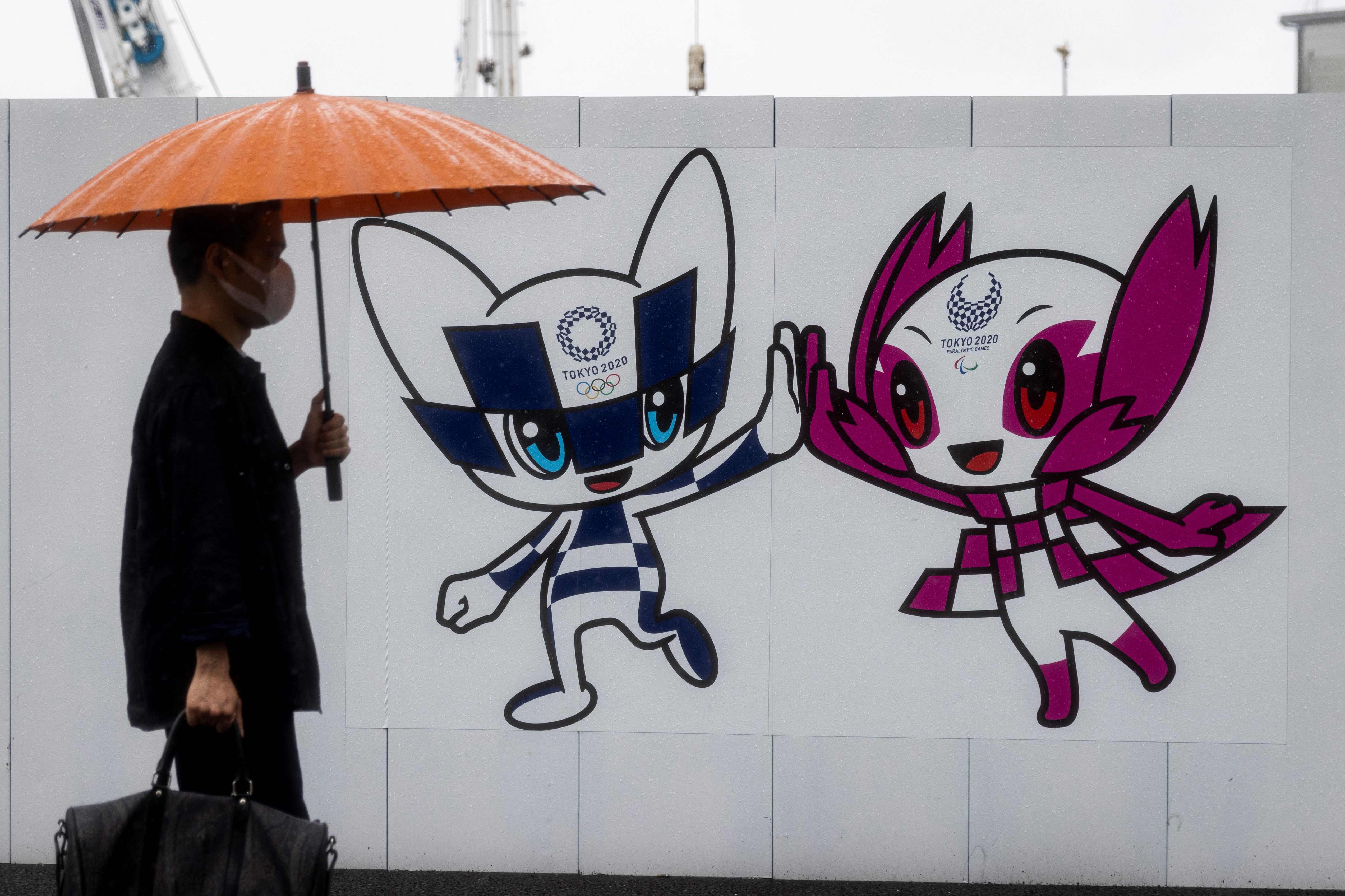 Seorang warga berjalan melintas di depan papan bergambar maskot Olimpiade Tokyo 2020.