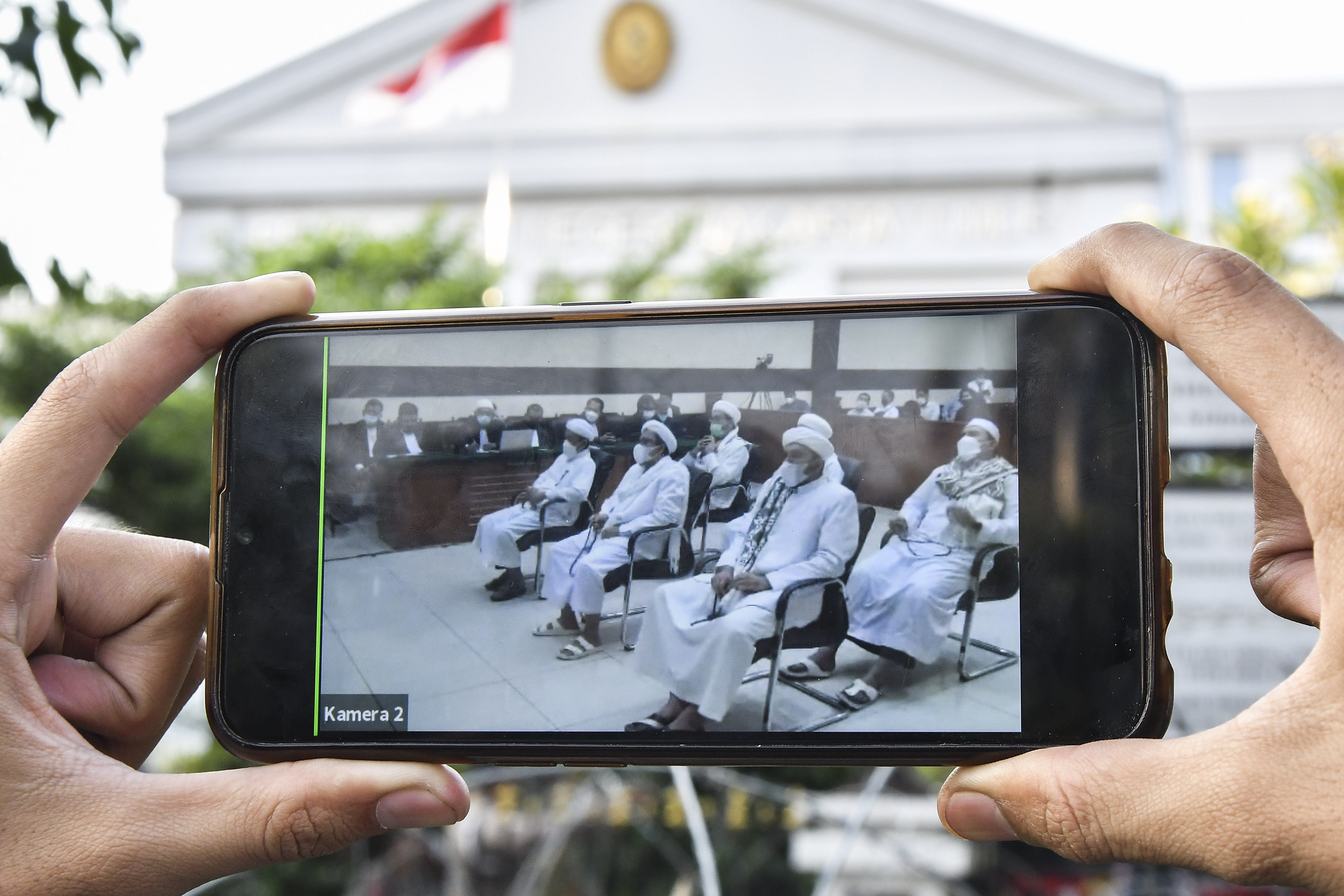 Jurnalis mengamati layar ponsel yang menampilkan sidang yang dihadiri Muhammad Rizieq Shihab di Pengadilan Negeri Jakarta Timur.