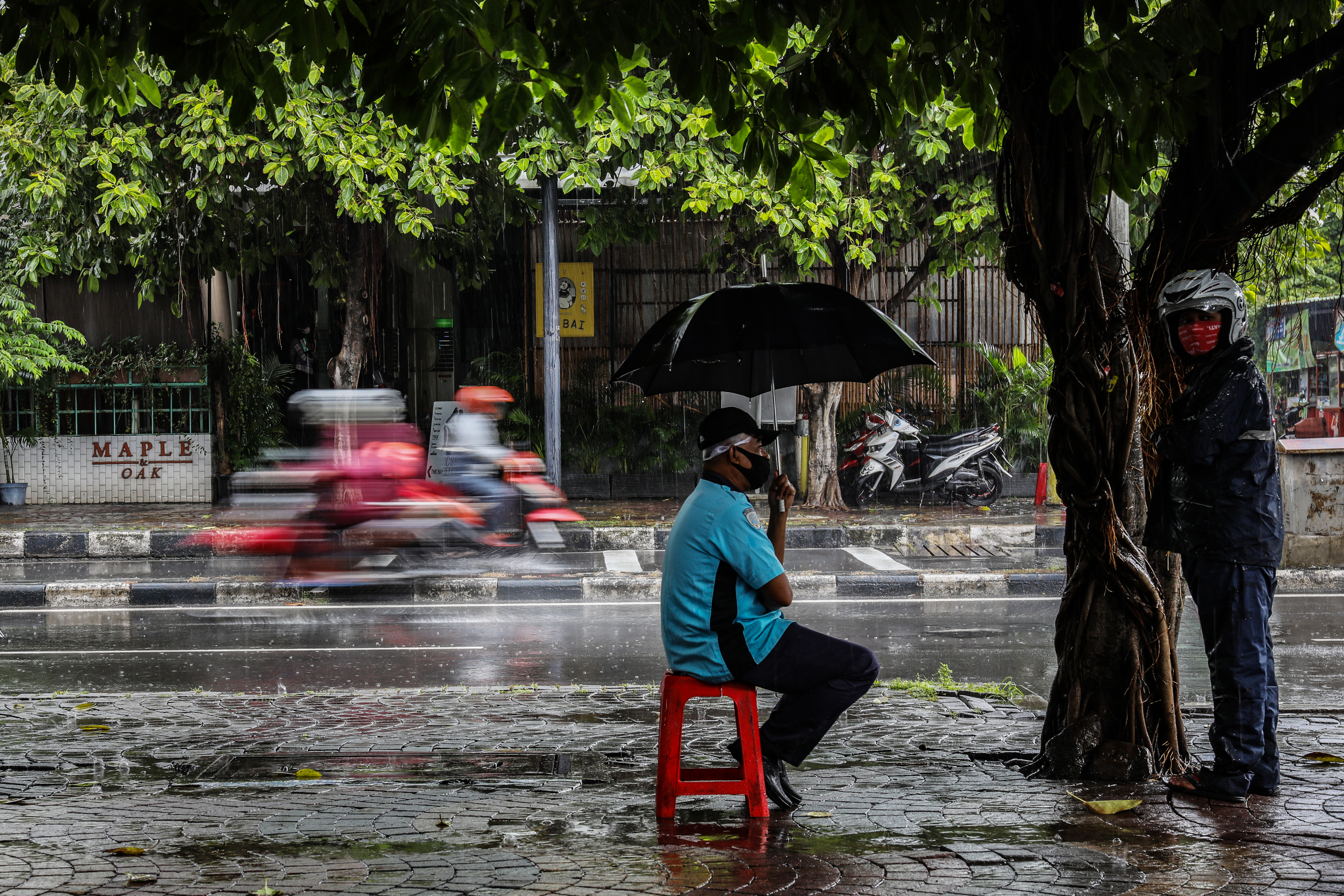 Petugas parkir mengenakan payung untuk menahan hujan di trotoar kawasan Menteng Jakarta Pusat.