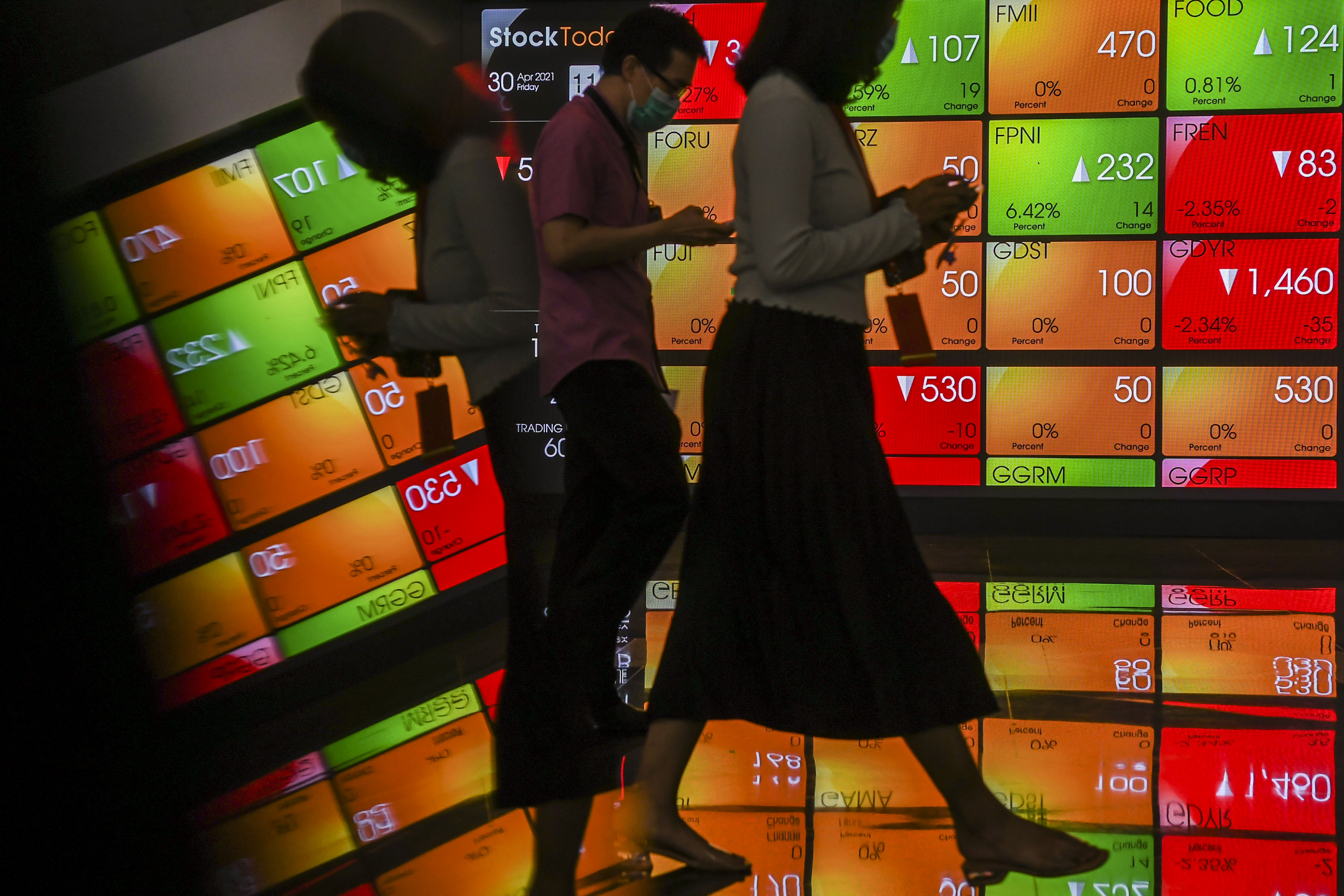 Pekerja melintas dengan latar belakang layar pergerakan harga saham di Bursa Efek Indonesia, Jakarta, Jumat (30/4).