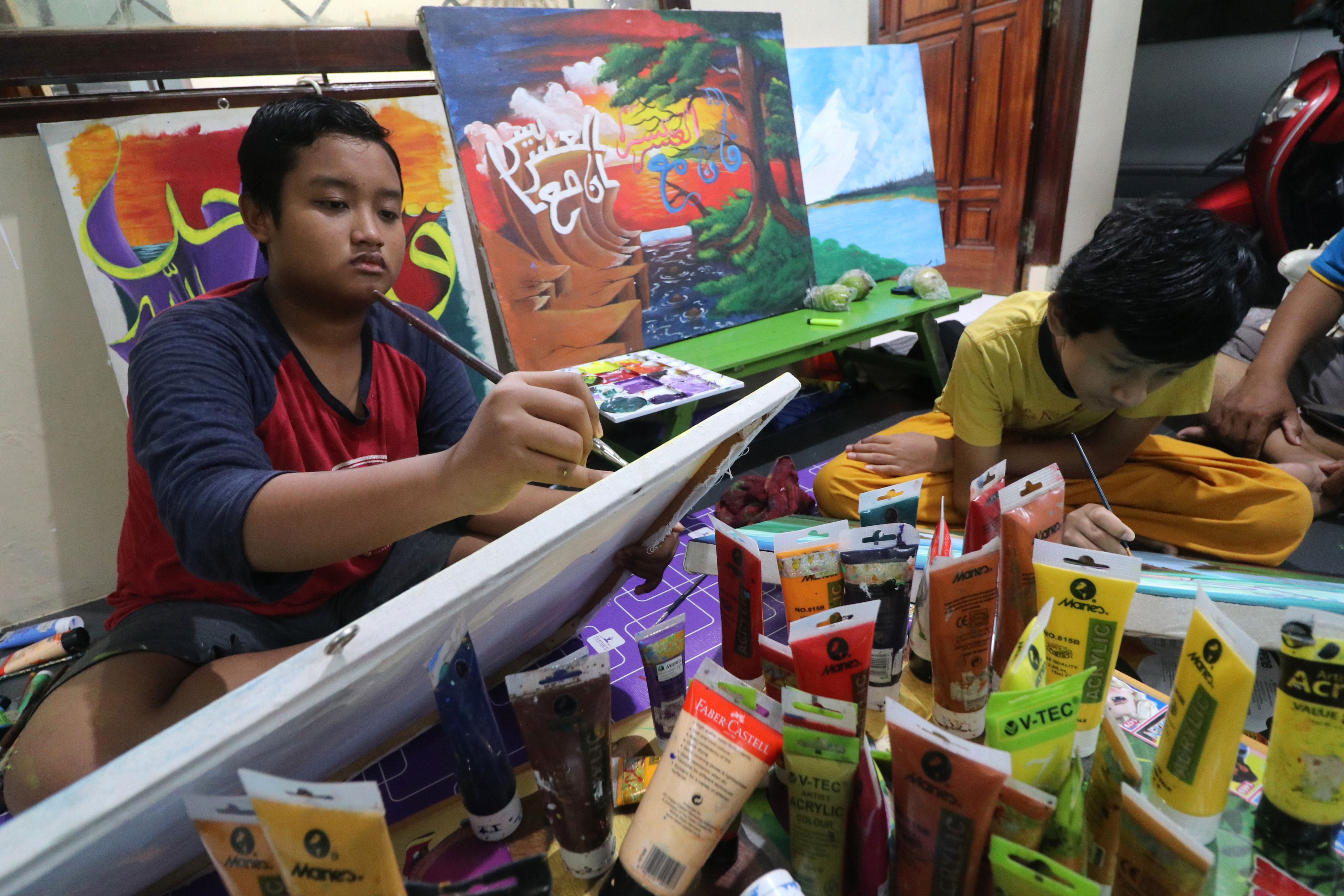Dua orang anak belajar melukis dengan bimbingan orang tuanya.