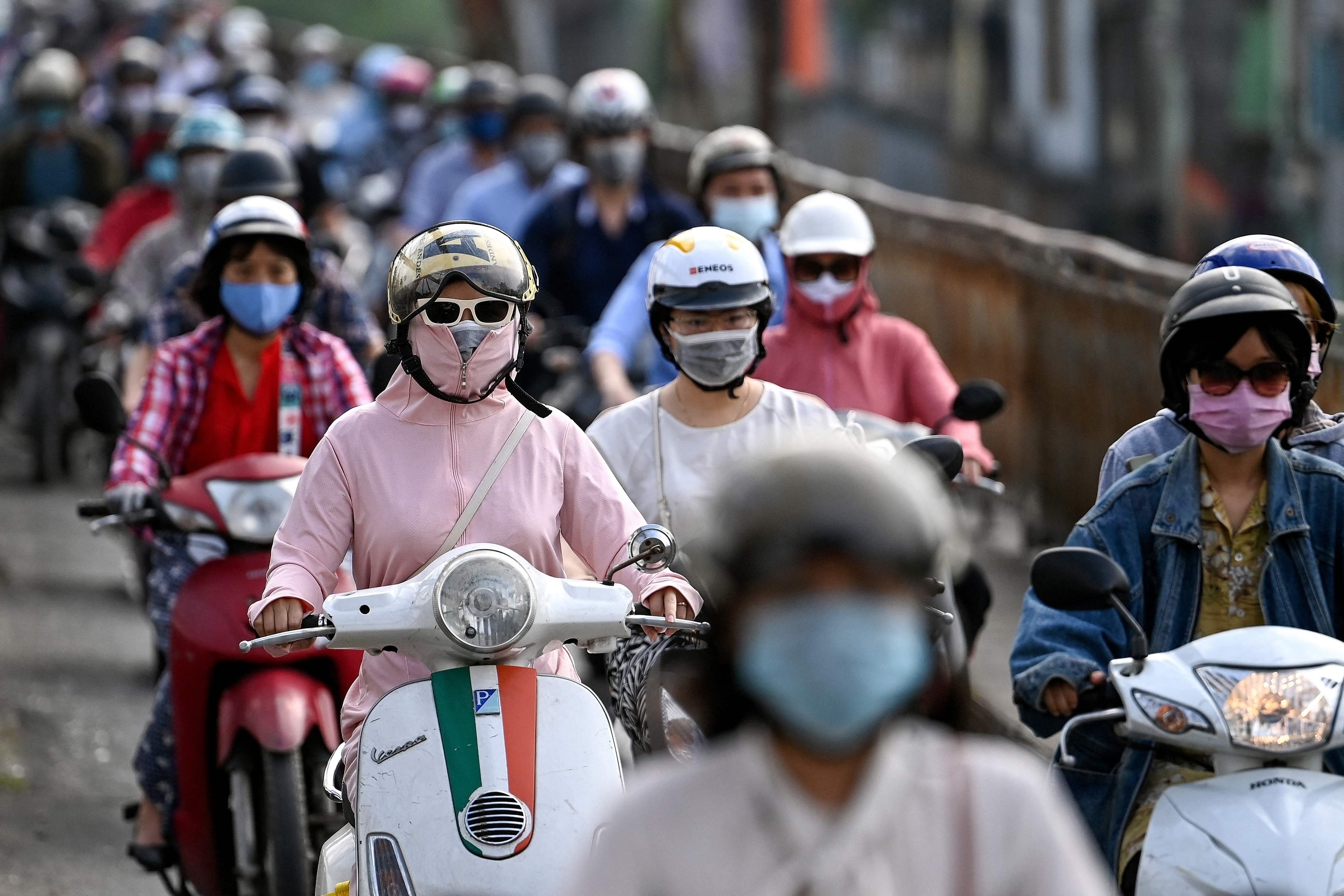 Pengendara sepeda motor mengenakan masker di Hanoi, Vietnam.