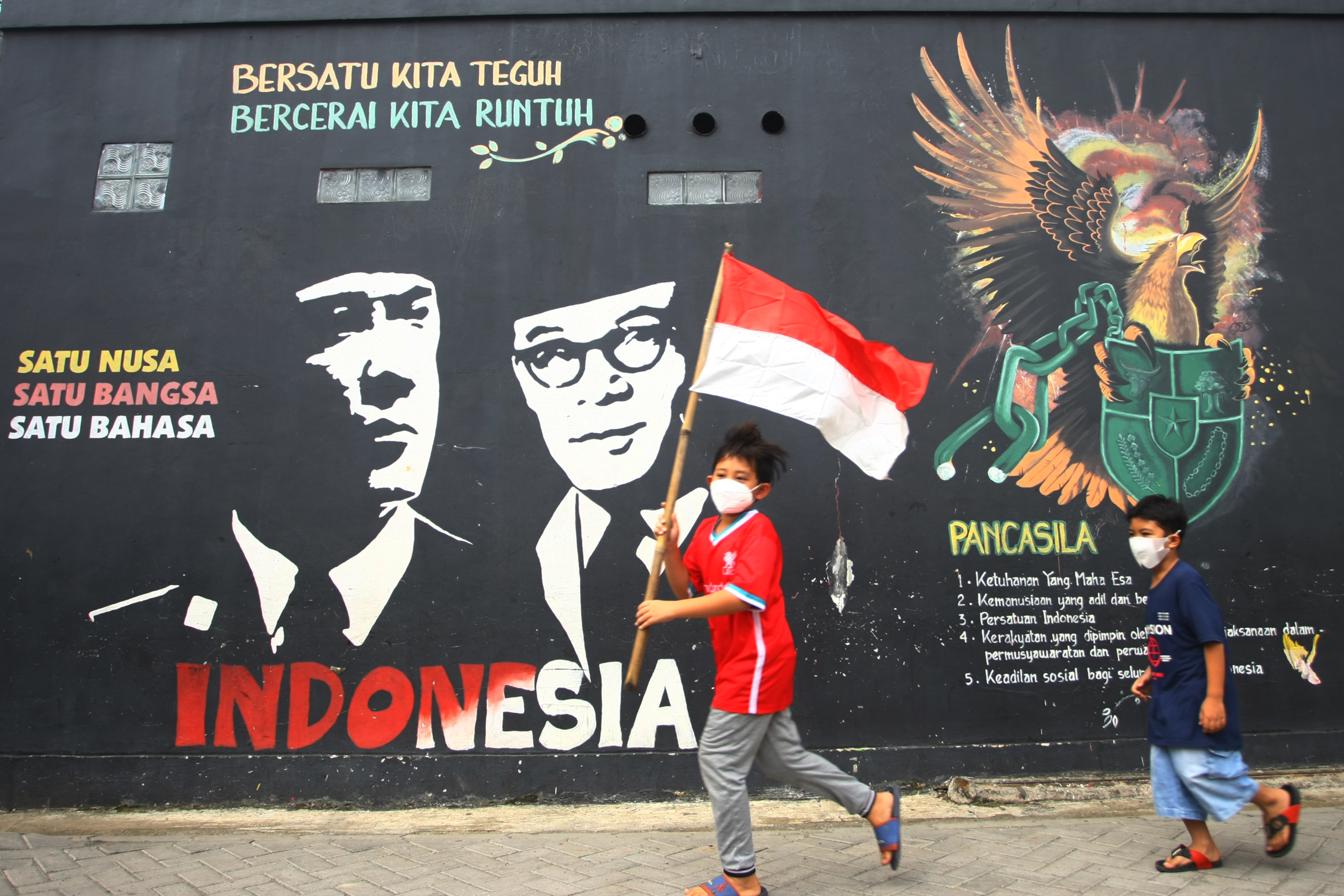 Dua bocah berlari mengibarkan bendera Merah Putih dalam peringatan Hari Lahir Pancasila.