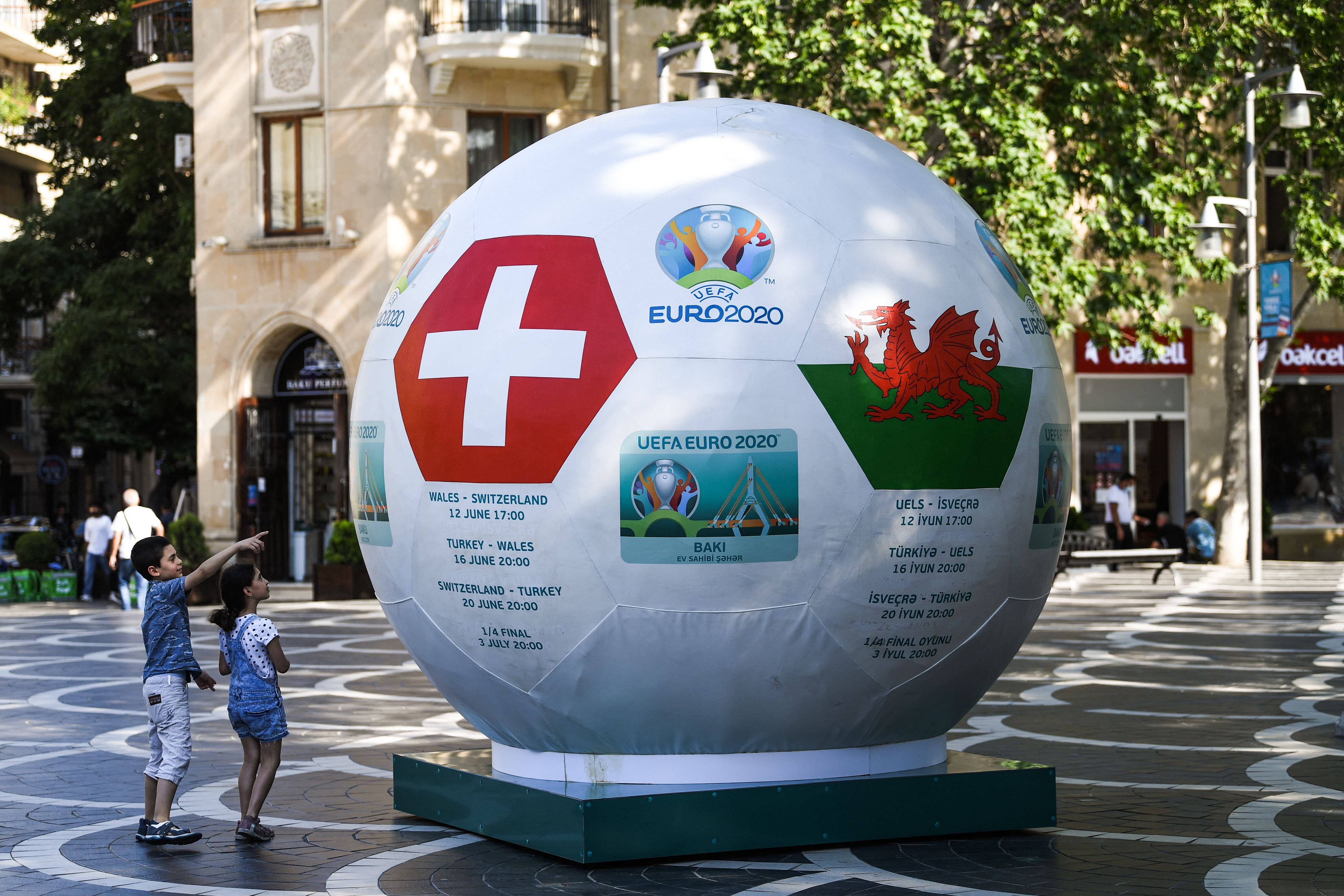 Dua anak berdiri di dekat bola yang menampilkan bendera Swiss dan Wales menjelang laga Piala Eropa di Baku, Azerbaijan.