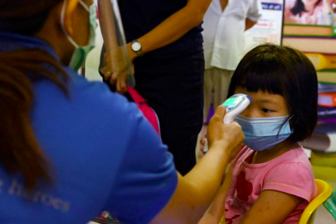 Seorang guru di Singapura mengecek suhu tubuh anak murid sebelum memulai pelajaran di kelas. Sekolah mulai dibuka 2 Juni 2020. 
