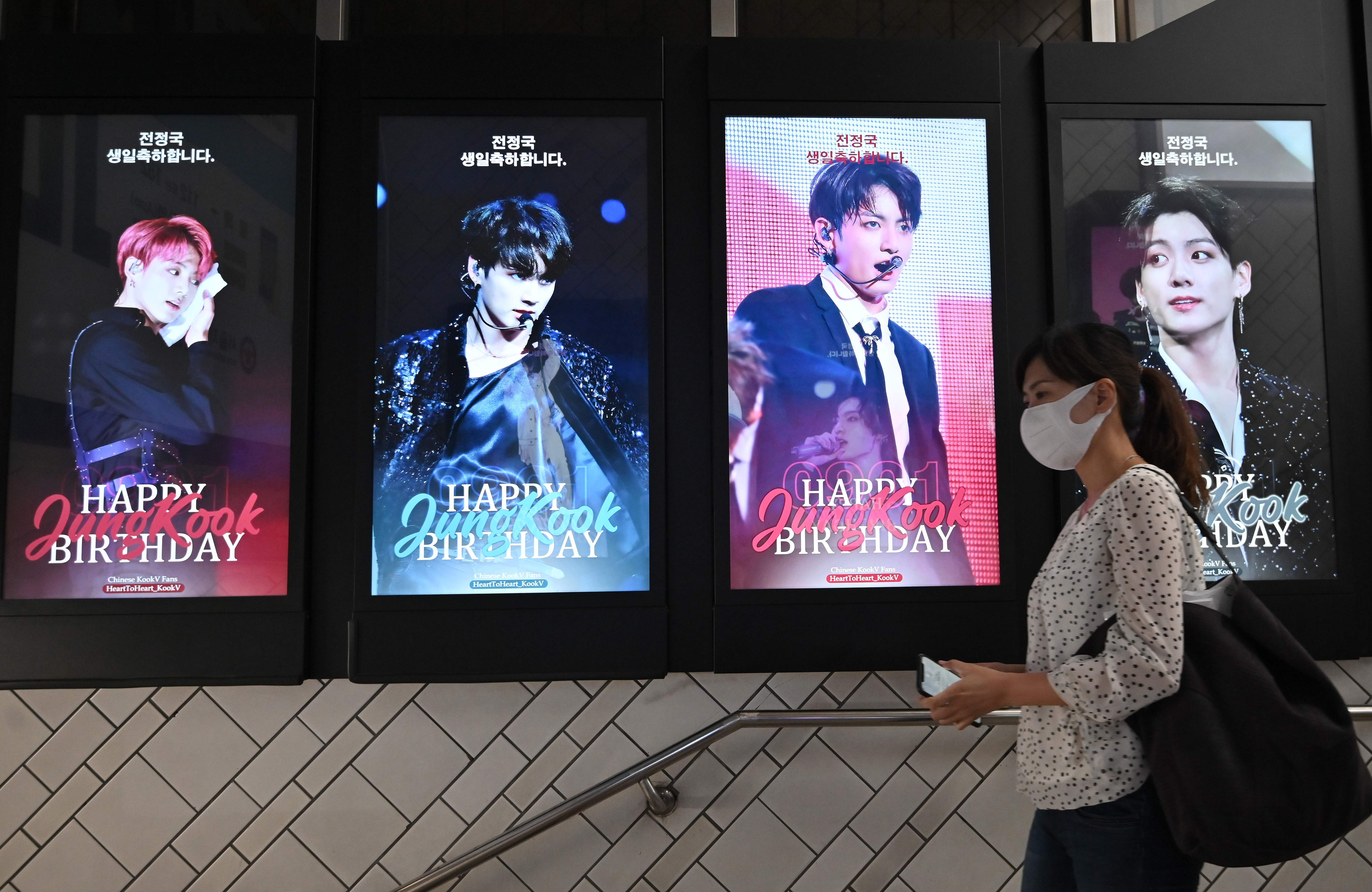Seorang warga melintasi papan elektronik yang menampilkan foto anggota BTS Jungkook.