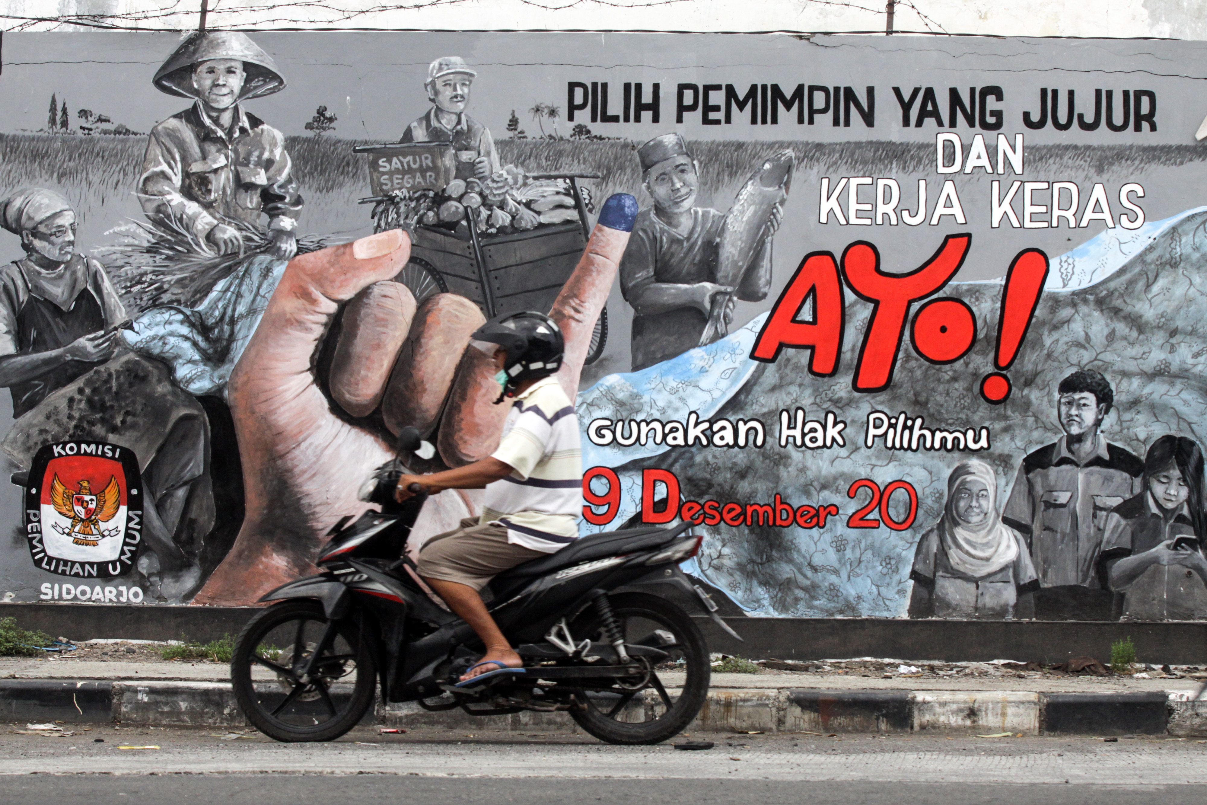 Pengendara melintas di depan mural bertema Pilkada 2020 di Jawa Timur.