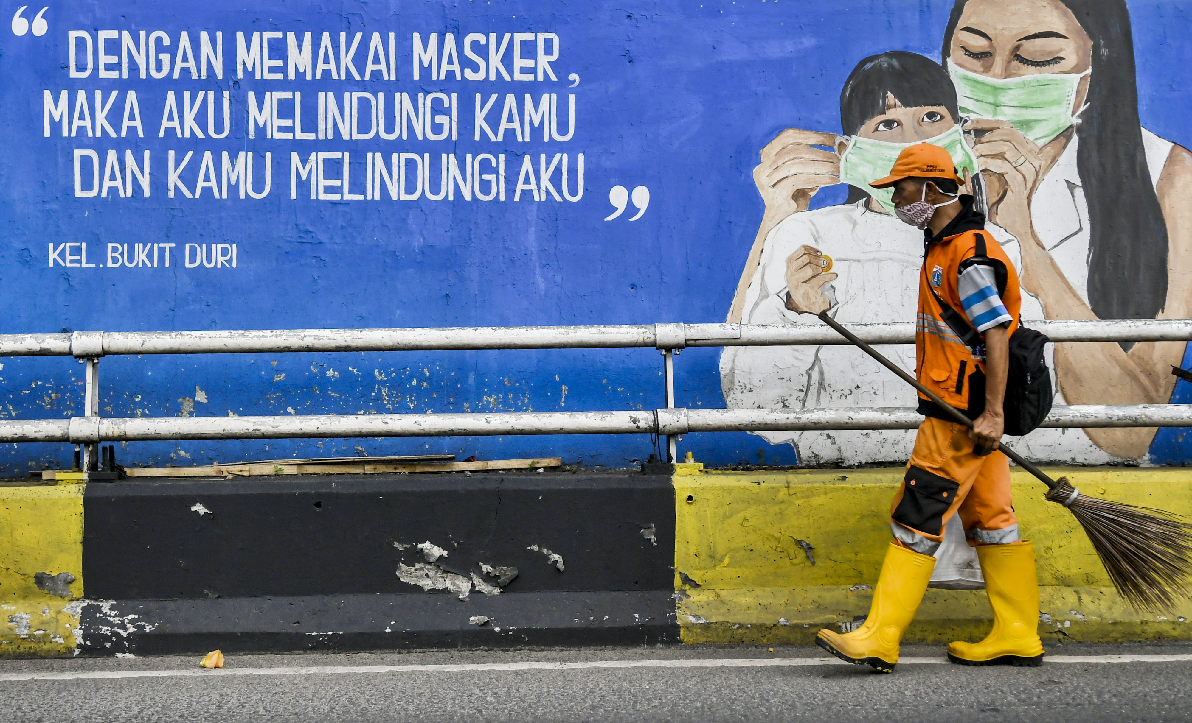 Petugas kebersihan melintasi mural tentang pandemi covid-19 di Kawasan Tebet, Jakarta.