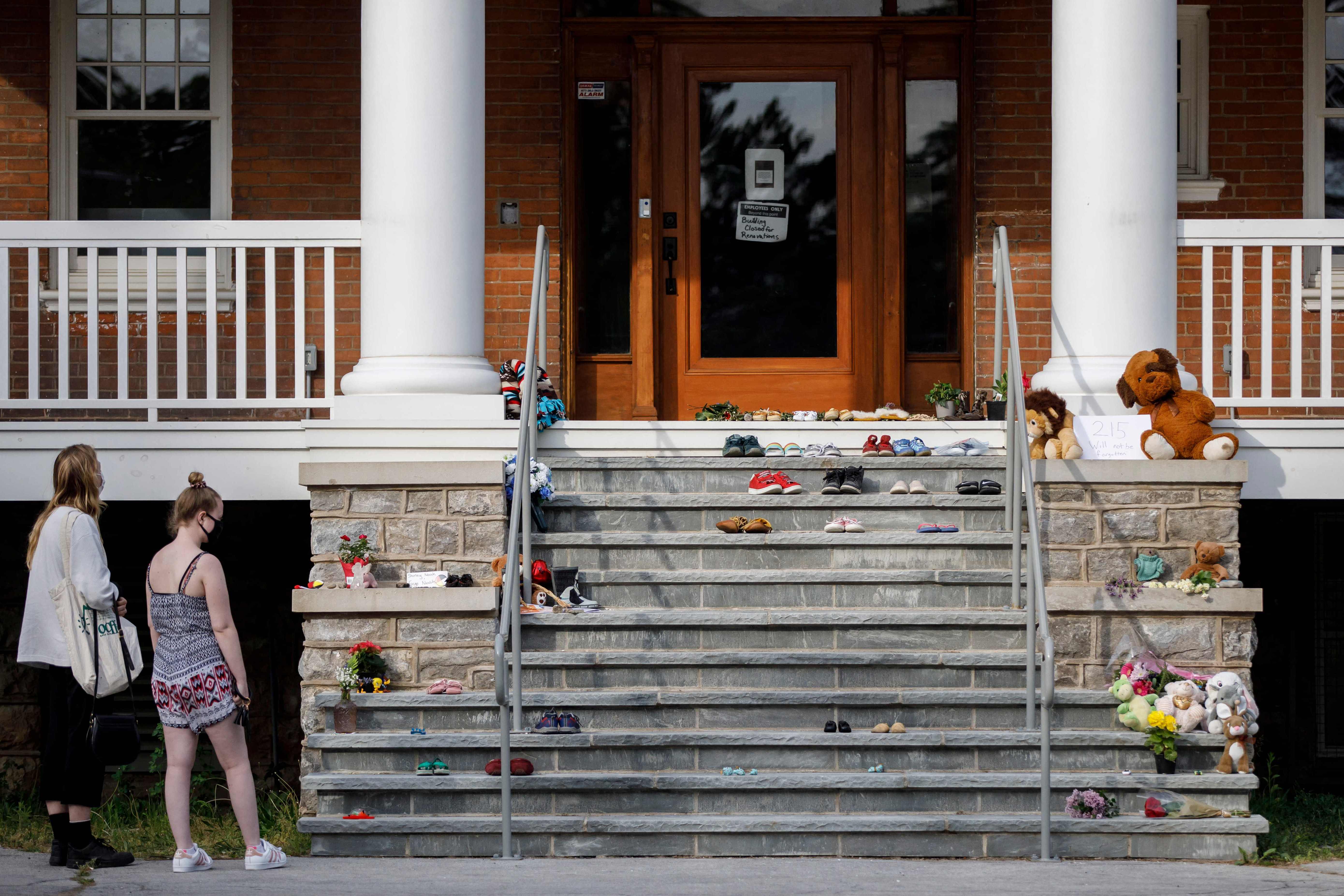 Orang-orang berdiri di depan tempat peringatan darurat untuk menghormati 215 anak yang jasad mereka baru-baru ini ditemukan.