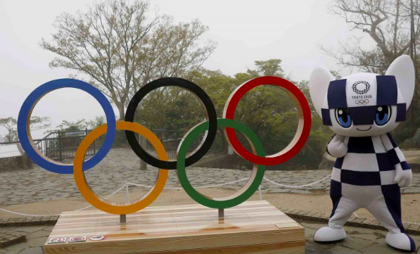 Salah satu maskot Olimpiade dan Paralimpik Tokyo 2020 Miraitowa berpose di samping lambang olimpiade.
