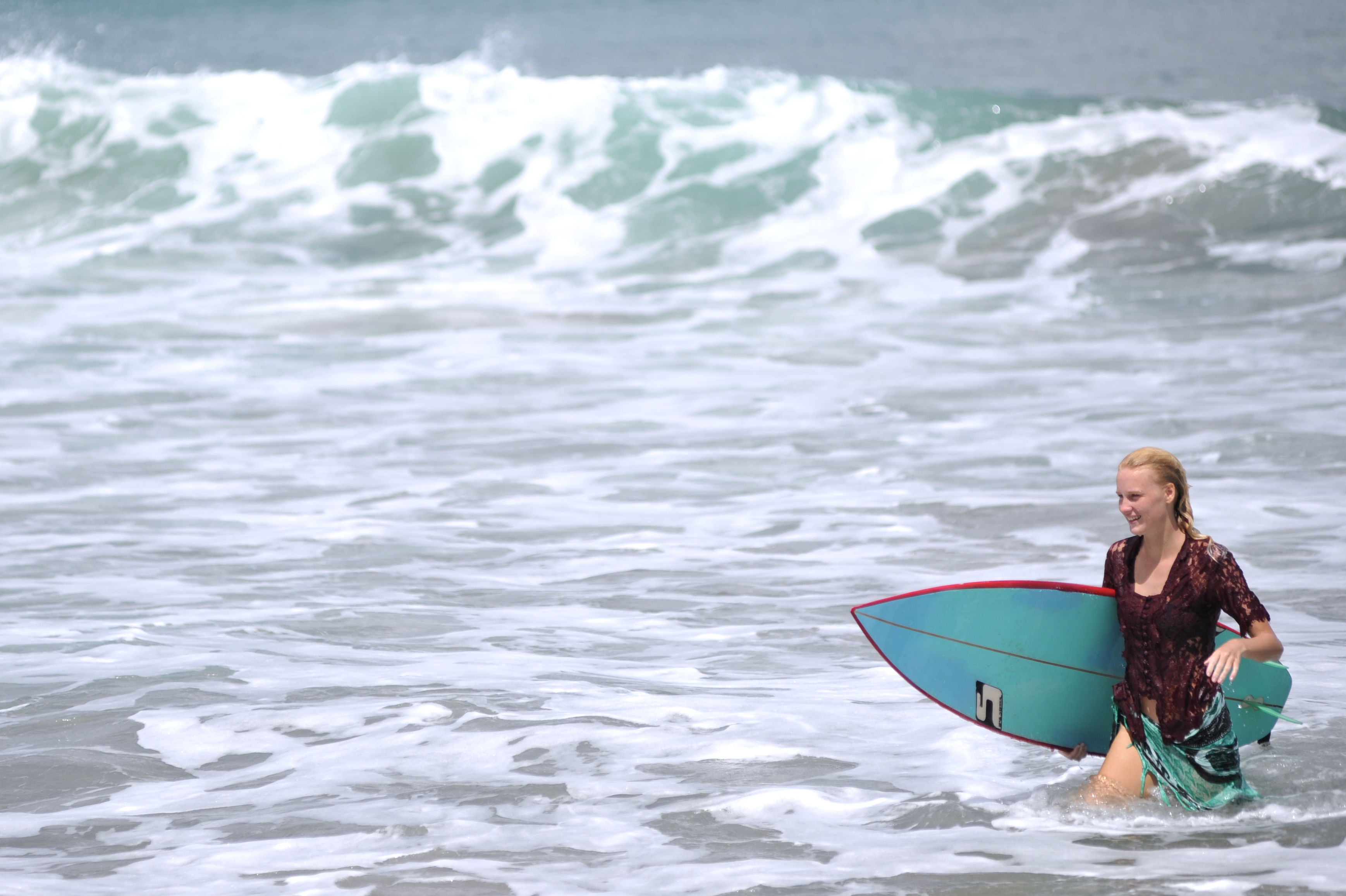 Seorang warga negara asing (WNA) yang mengenakan busana kebaya membawa papan selancar di Pantai Kuta, Badung, Bali