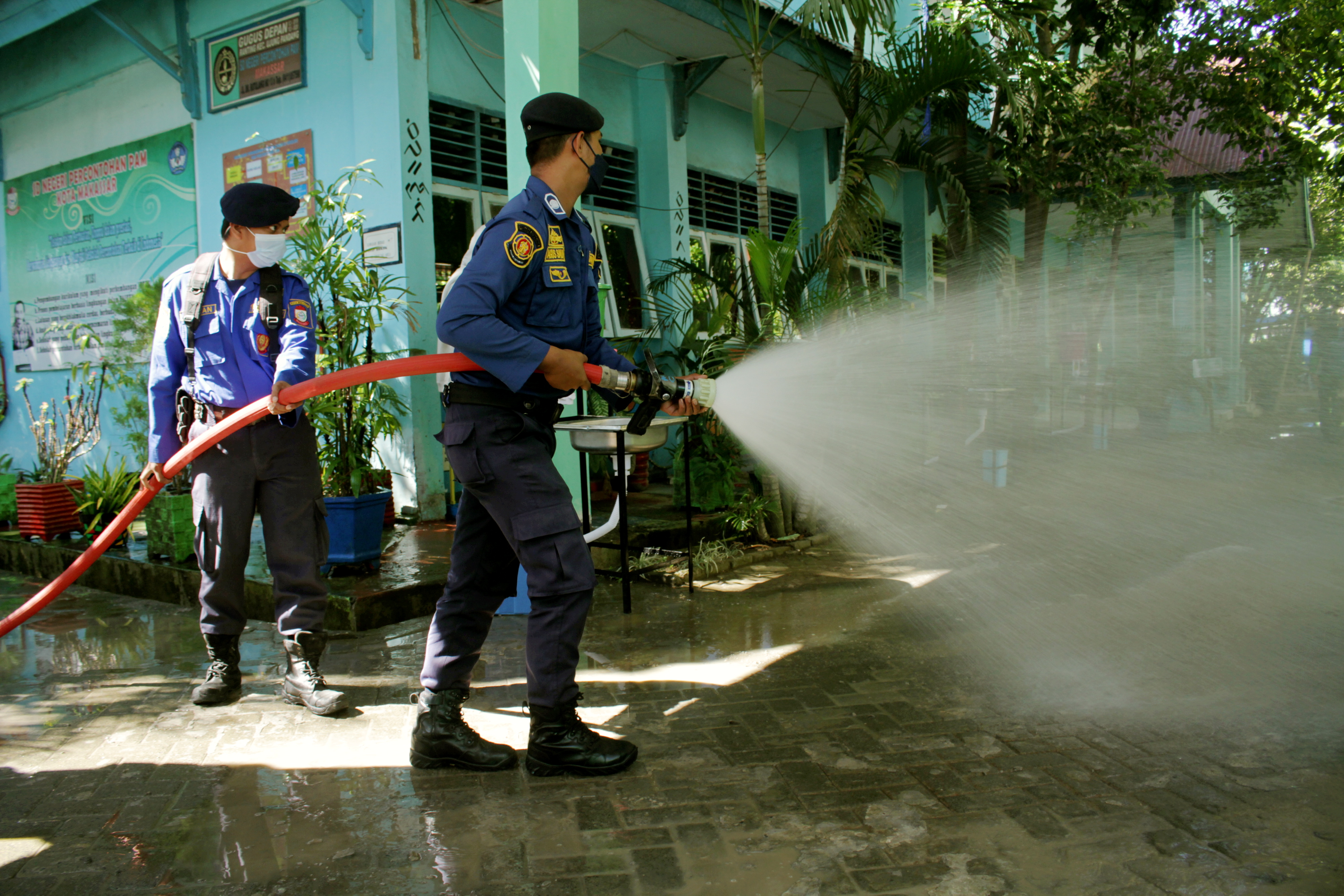 Petugas pemadam kebakaran menyemprotkan cairan disinfektasn di Sekolah Negeri Percontohan PAM di Makassar, Sulawesi Selatan.