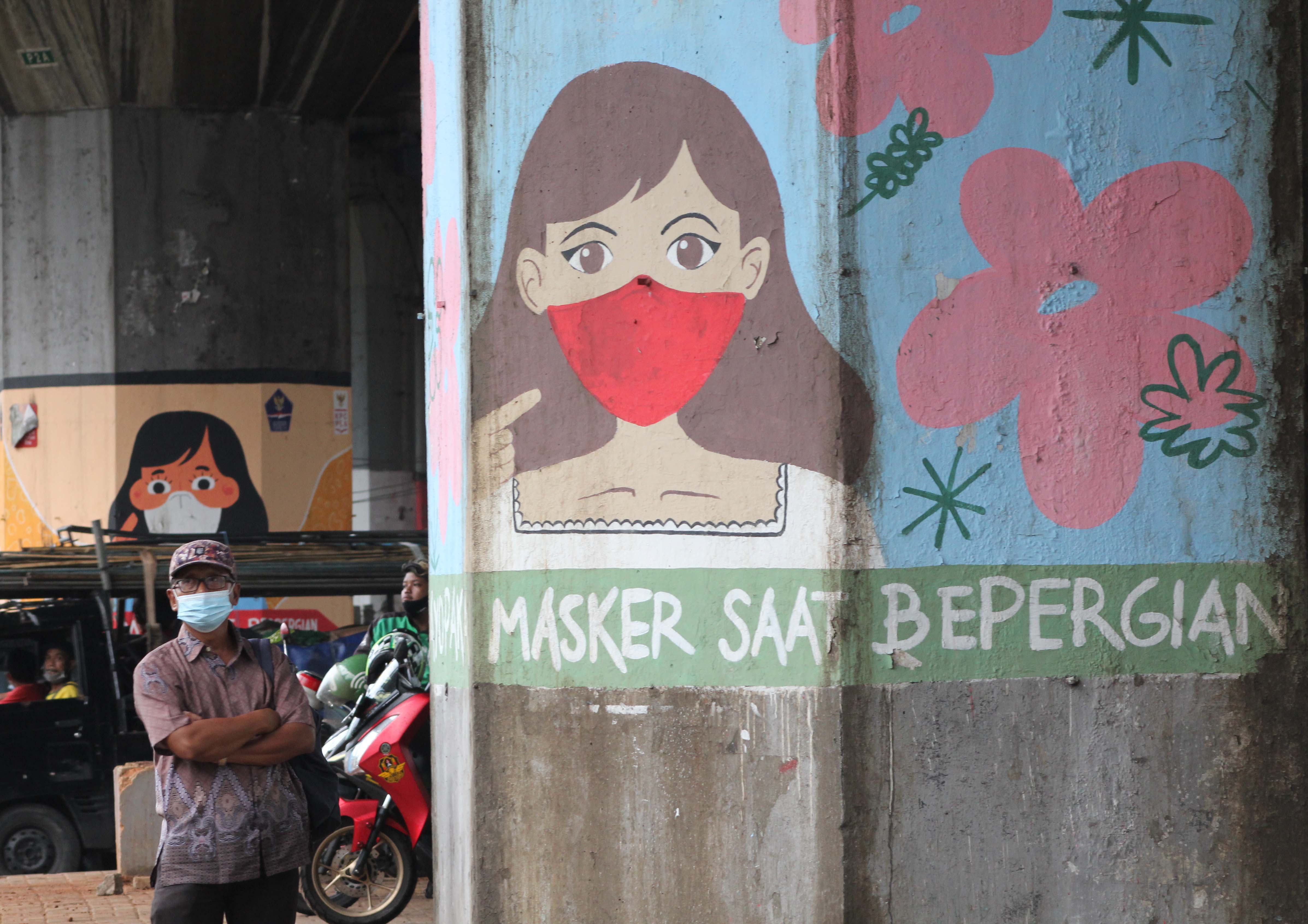 Pengendara kendaraan bermotor melintasi Mural Sosialisasi Penularan Covid-19 di Jalan DI Panjaitan, Jakarta.