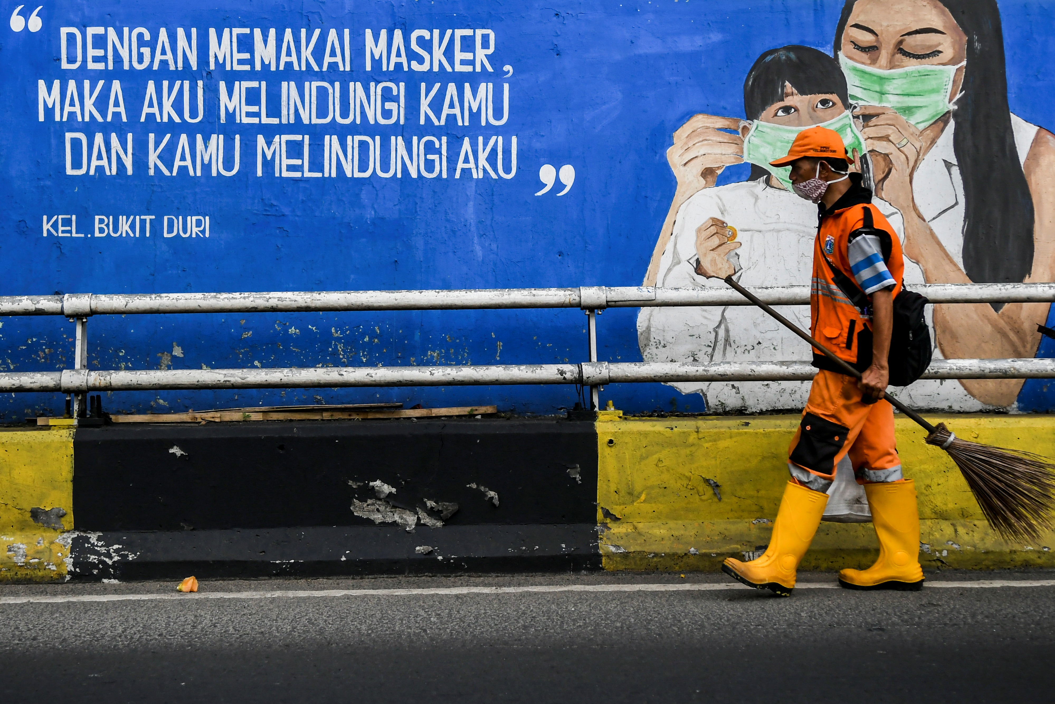 Petugas kebersihan melintas di depan mural tentang pandemi covid-19 di Kawasan Tebet, Jakarta.
