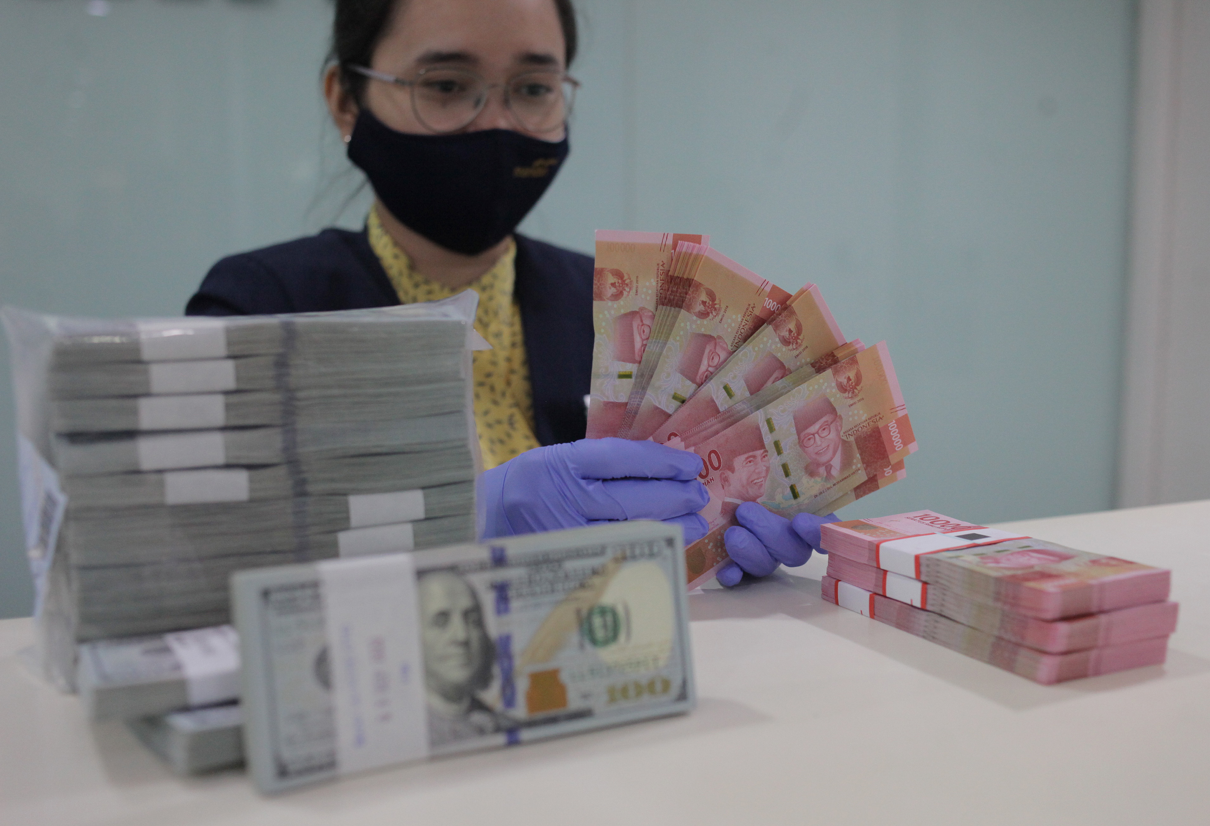 Ilustrasi karyawan bank menghitung uang rupiah dan dolar AS.