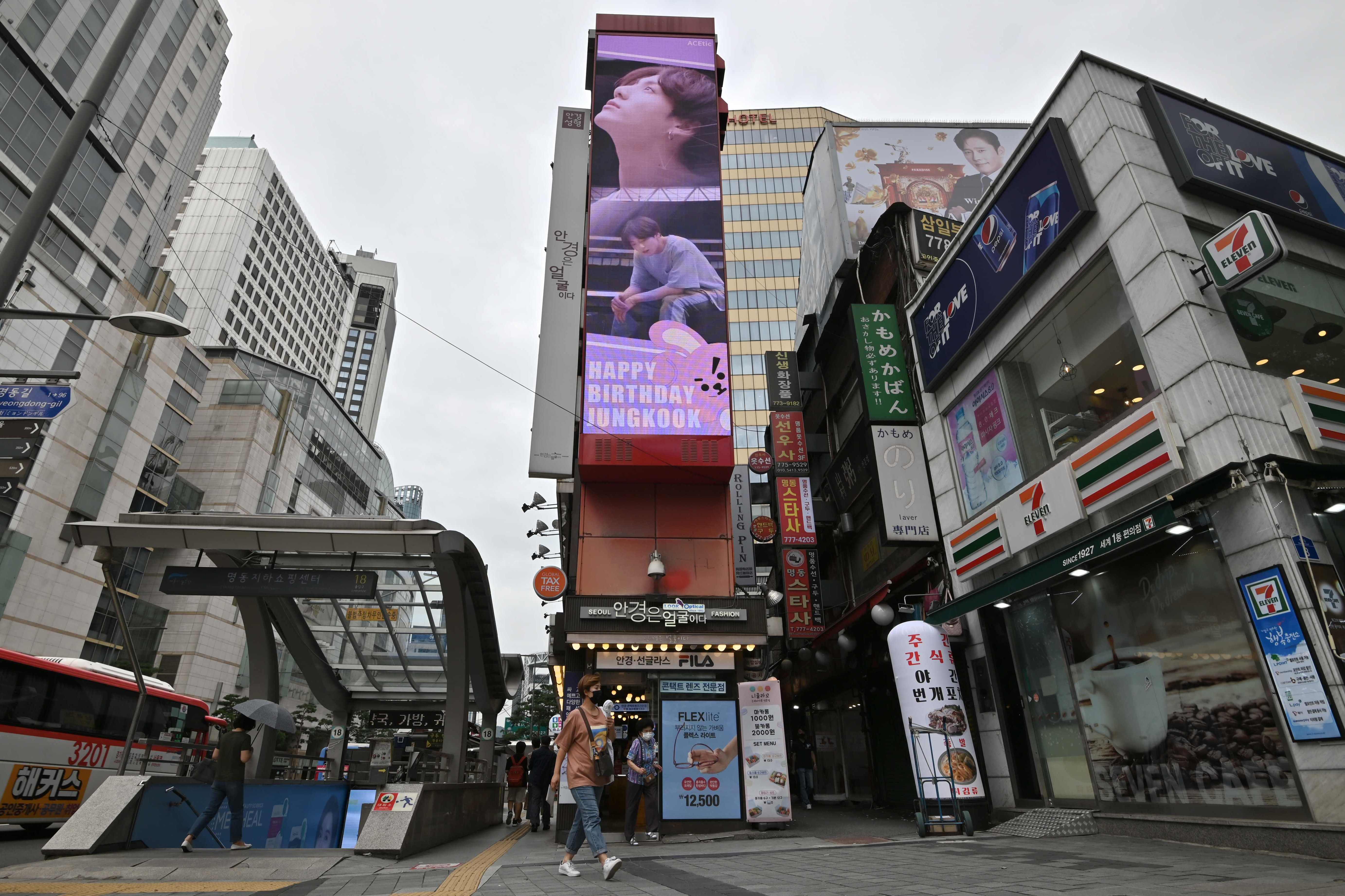 Seorang wanita berjalan melewati layar listrik besar (tengah) yang menunjukkan Jeon Jung-kook, anggota K-pop BTS, Seoul, Korsel.