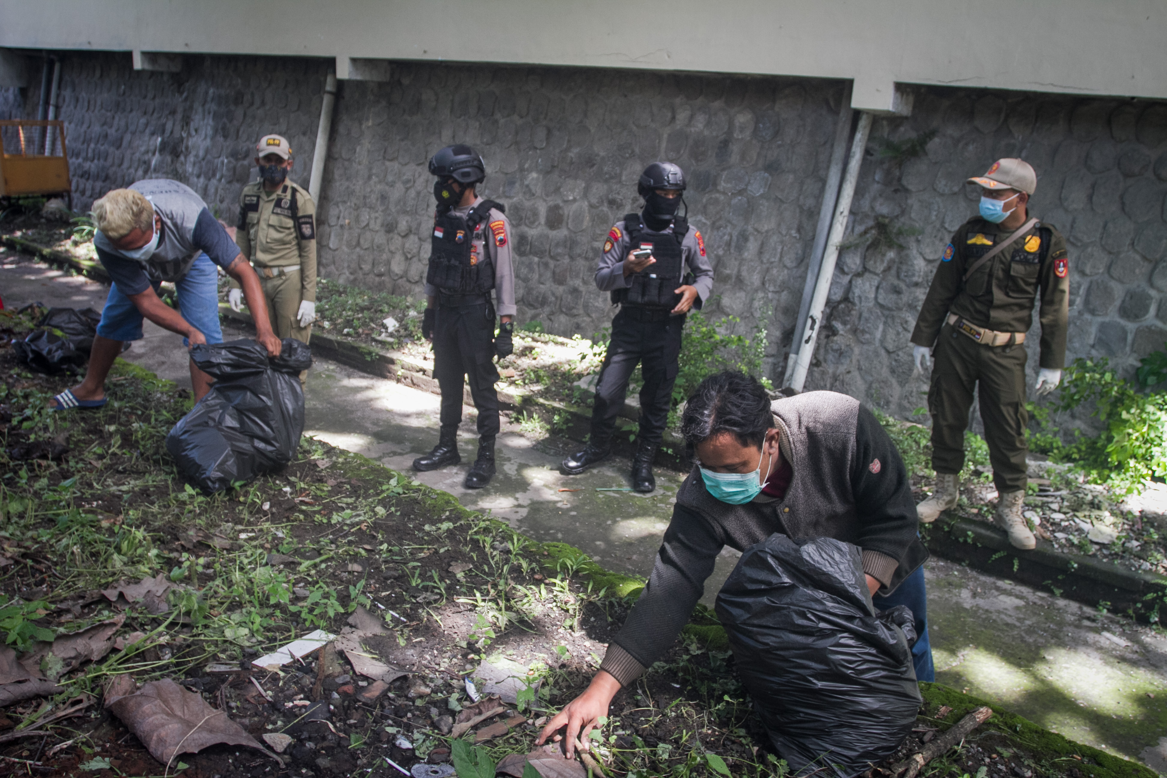 Tim gabungan menghukum warga yang tidak memakai masker dengan membersihkan sampah di Jalan Brigjen Sudiarto, Solo, Jawa Tengah.