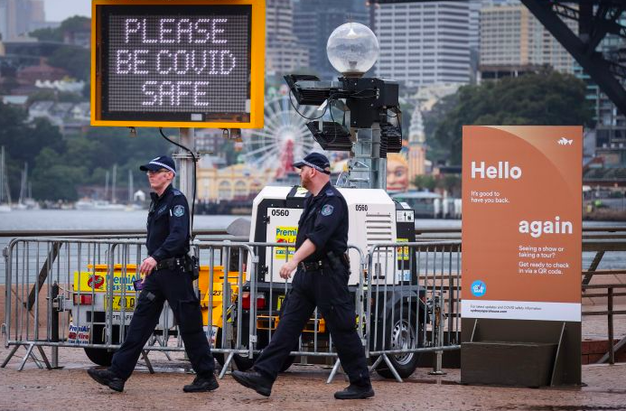 Dua polisi New South Wales melewati gedung dengan papa nama yang meminta cegah Covid-19 di Sydney, New South Wales, Australia.