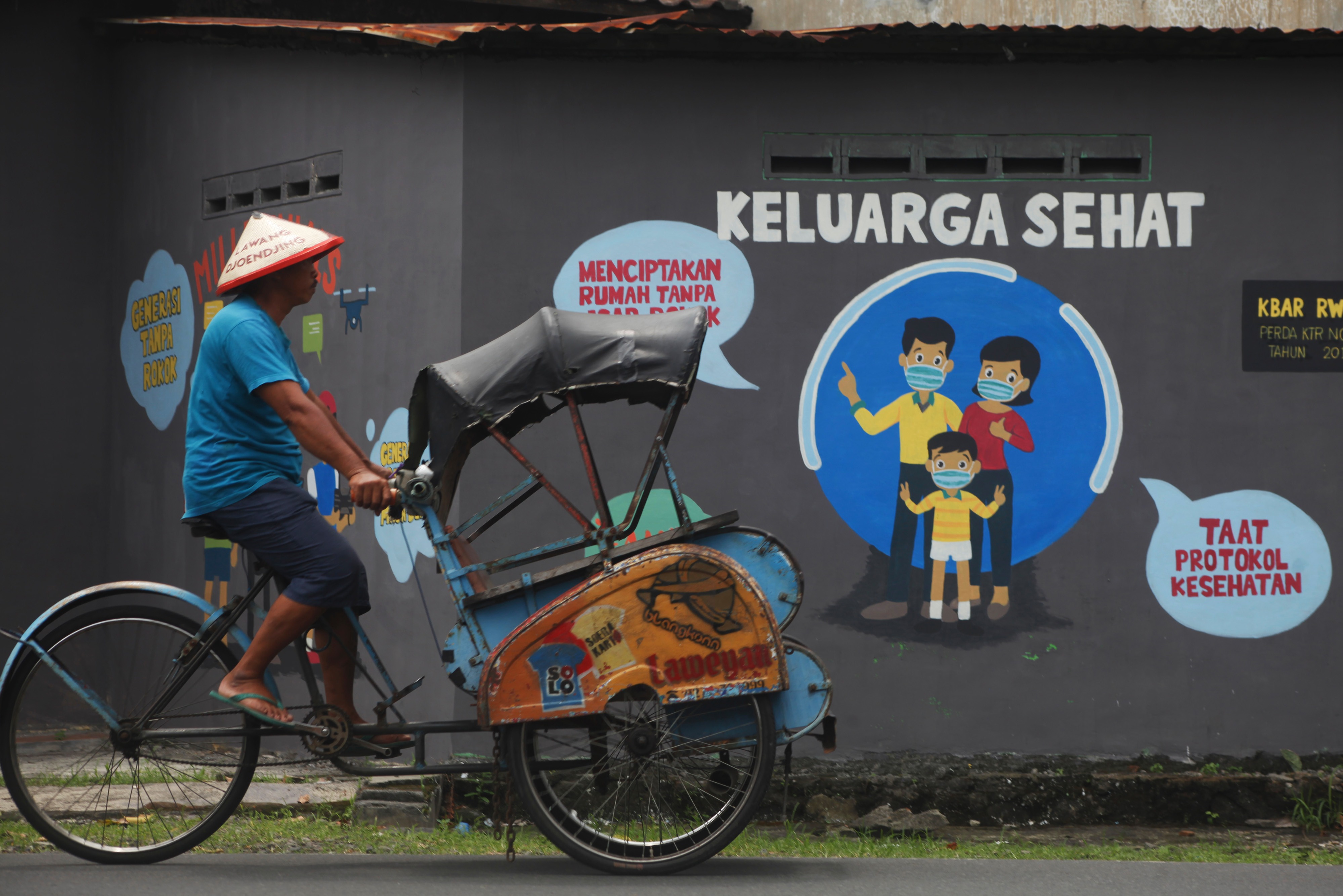 Warga melintas di depan mural edukasi kesehatan di kawasan Bibis, Banjarsari, Solo, Jawa Tengah.