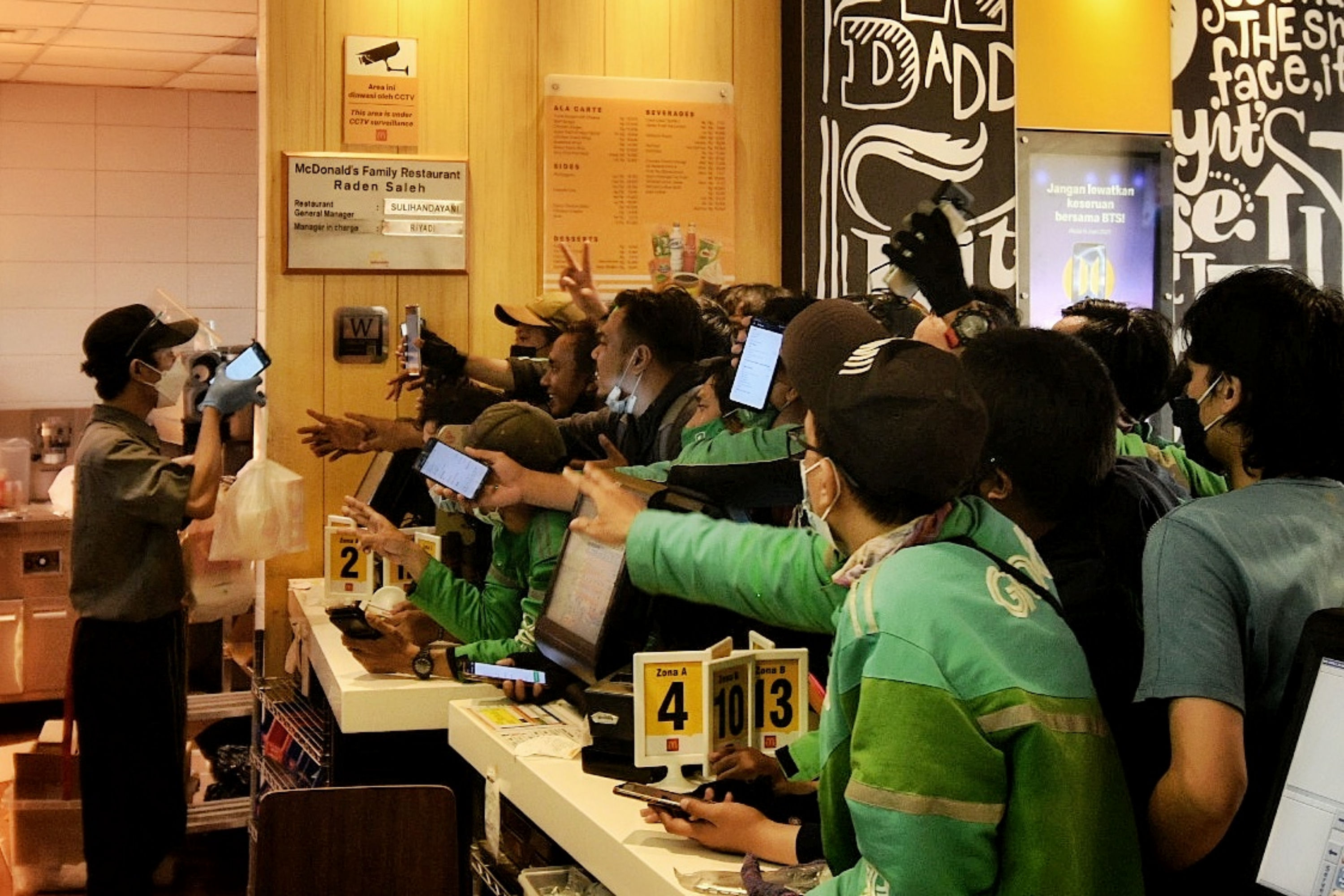 Pengemudi ojek online mengantre untuk mengambil pesanan makanan cepat saji tanpa menerapkan protokol kesehatan di gerai McDonald