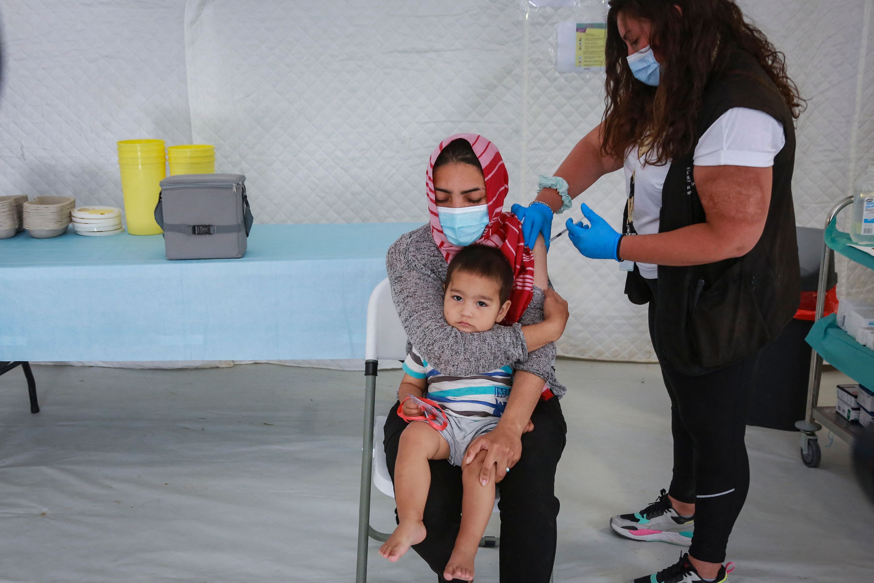 Seorang perempuan yang memangku anaknya menerima suntikan vaksin covid-19 di kamp pengungsian pencari suaka di Pulau Lesbos, Yunani.