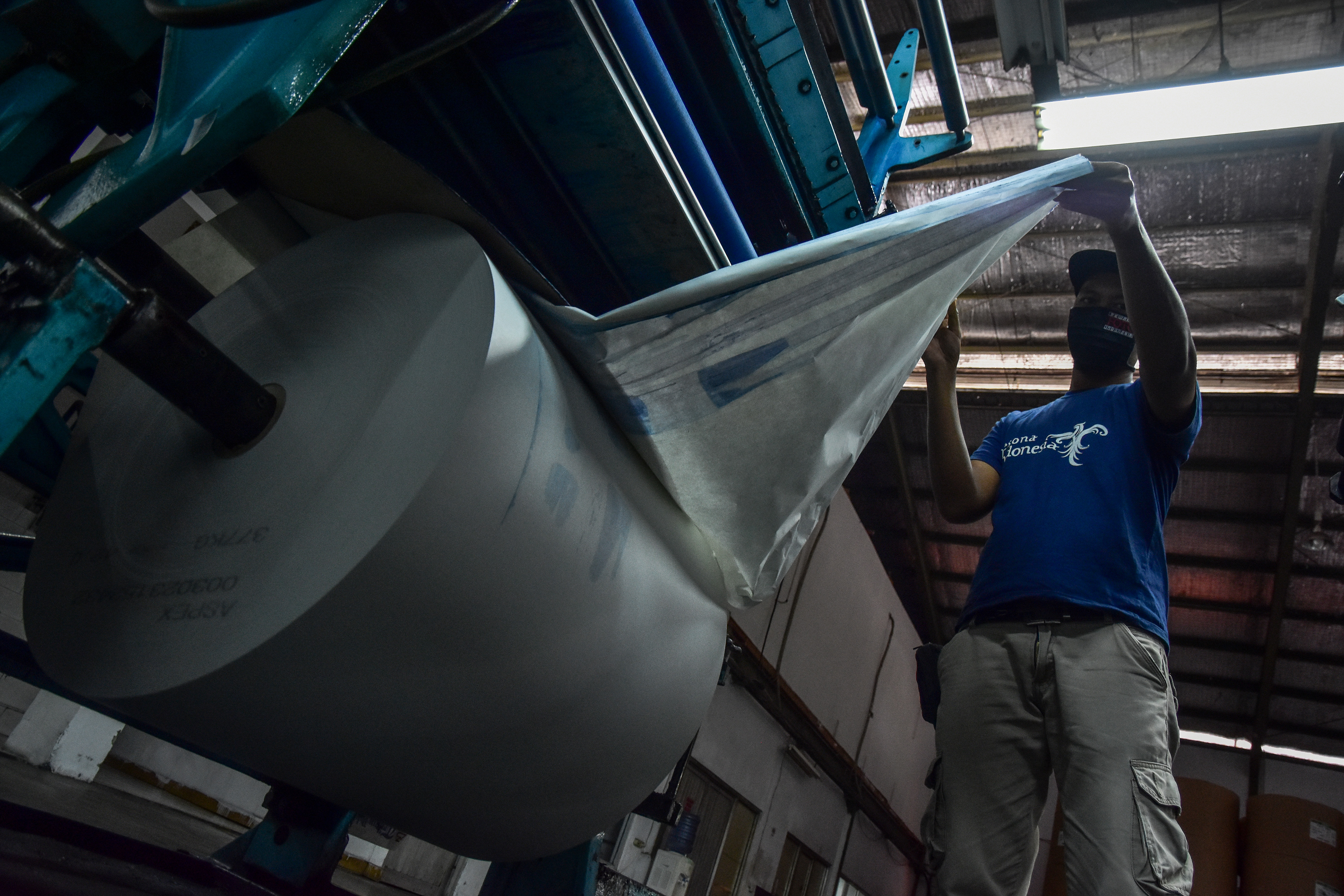 Seorang pegawai memeriksa kondisi mesin cetak dan kertasnya