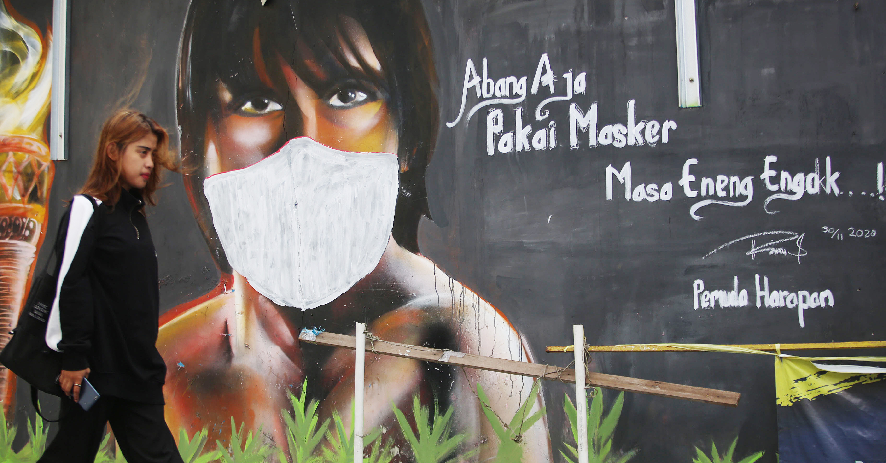 Ilustrasi: Warga yang tidak memakai masker melintas di depan mural berisi imbauan mengunakan masker di Jakarta