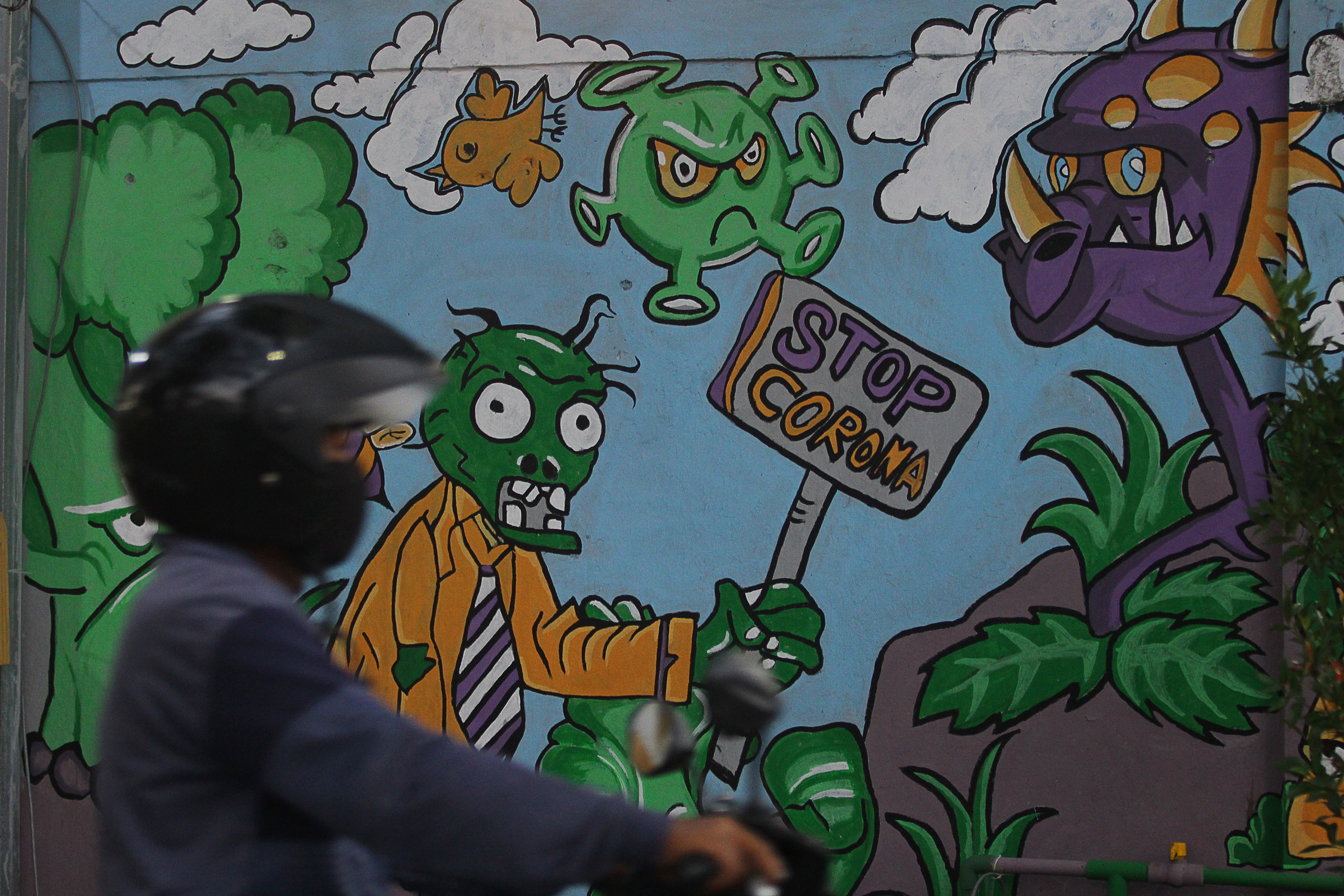 Pengendara sepeda motor melintas di depan mural Stop Corona di Kampung Jogoloyo, Surabaya, Jawa Timur.