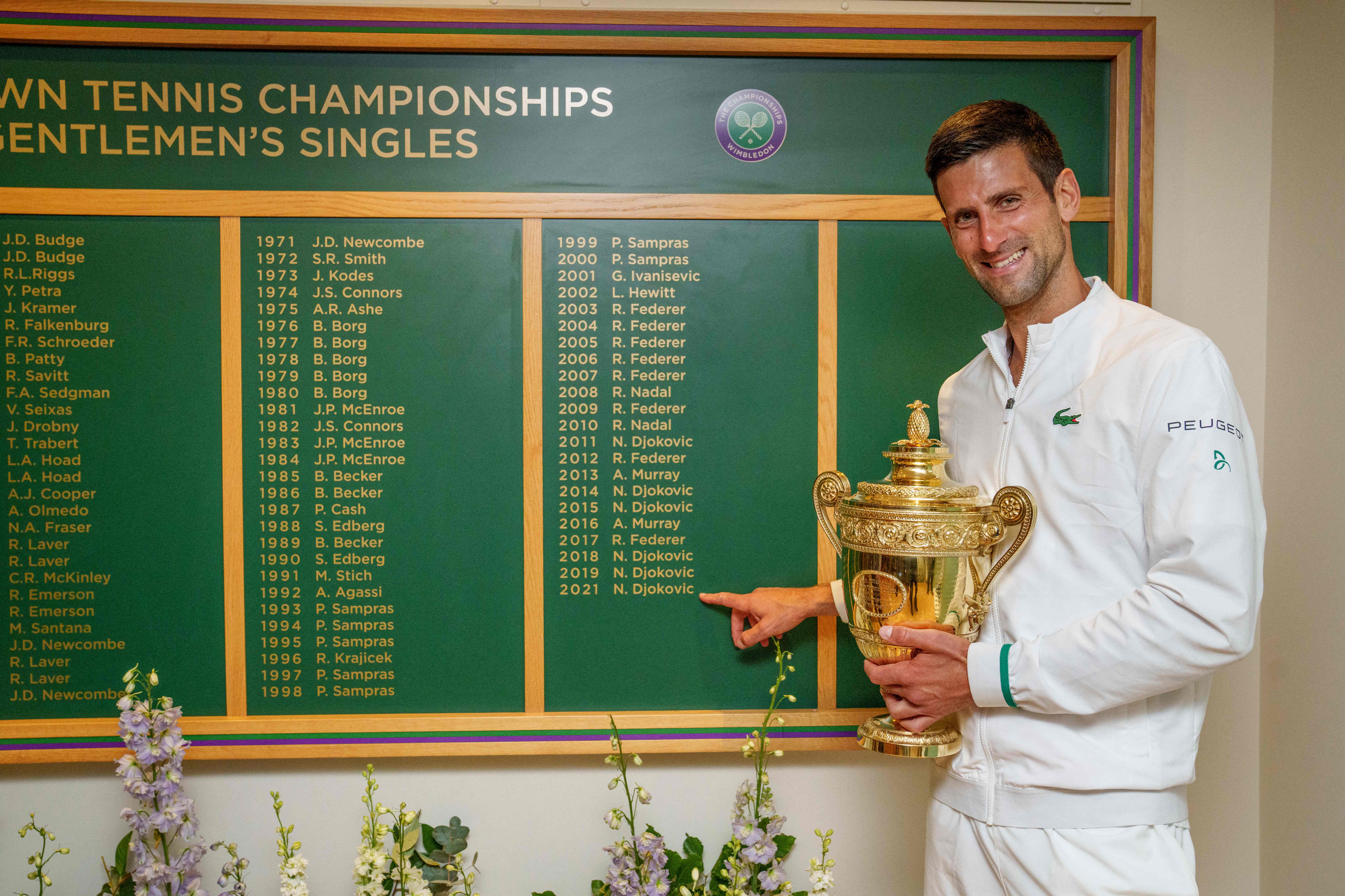 Petenis Serbia Novak Djokovic memegang trofi Wimbledon sembari menunjuk namanya di daftar juara turnamen Grand Slam itu.