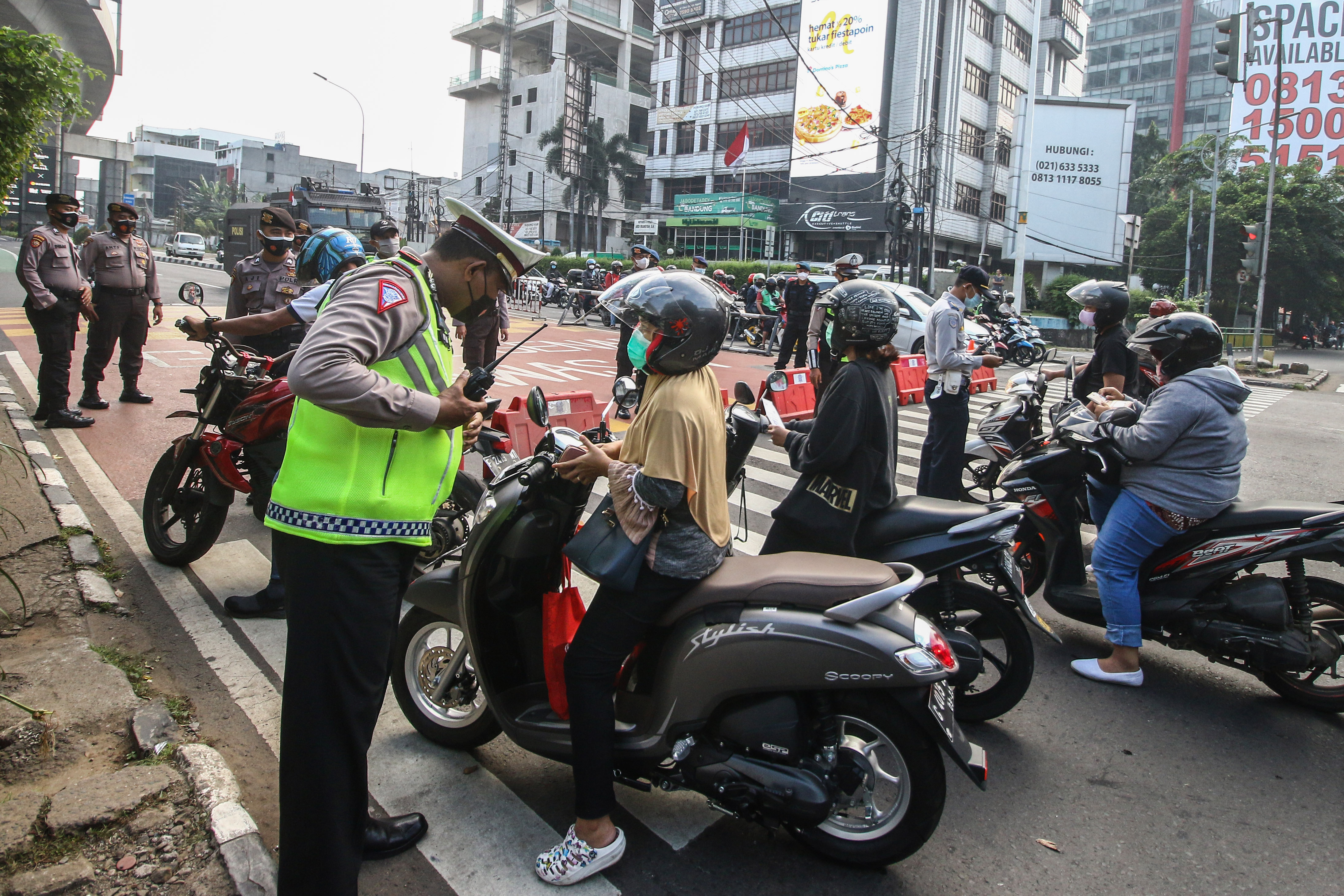 Petugas kepolisian saat memeriksa pengendara motor di titik penyekatan wilayah Jakarta.