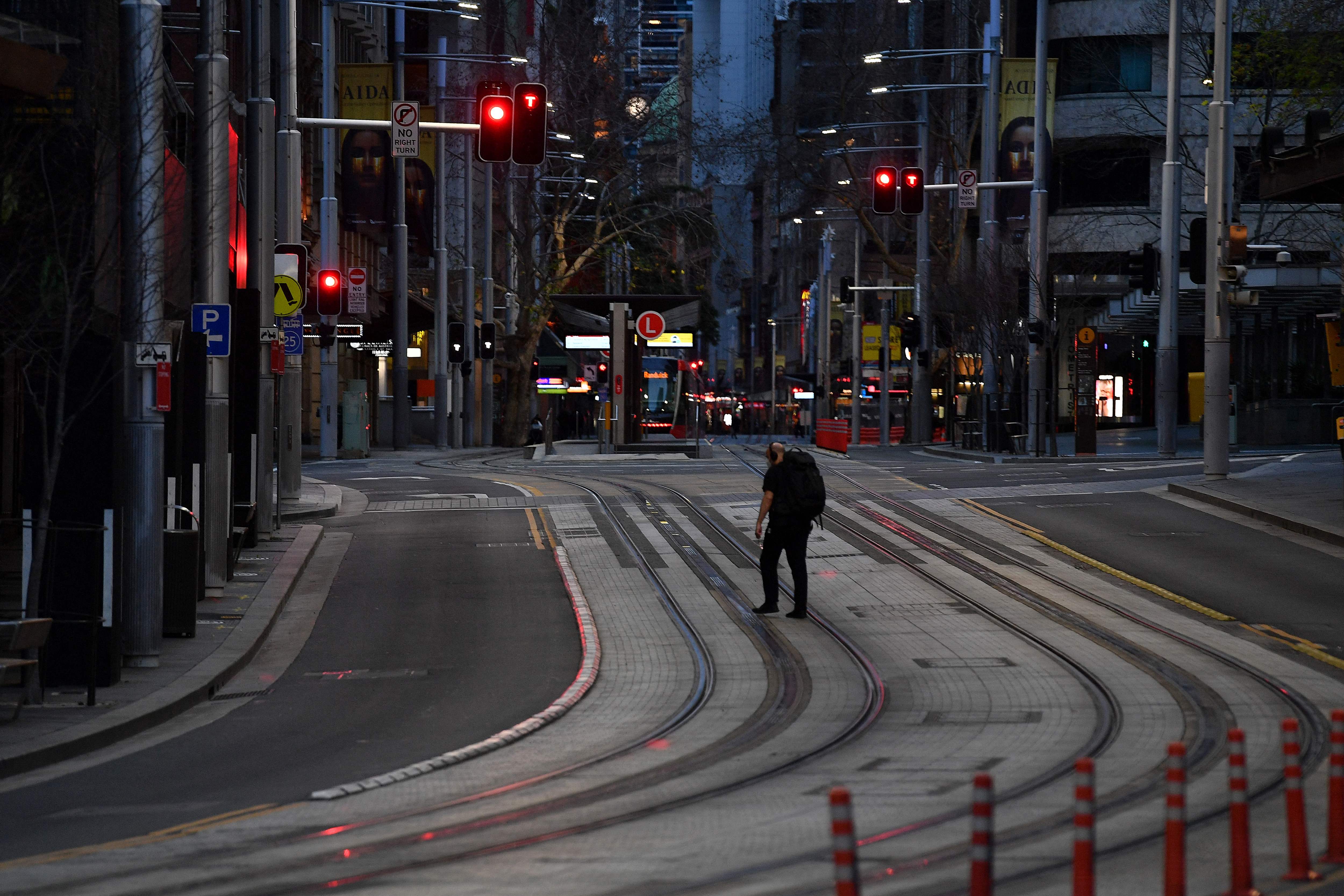 Seorang warga mengenakan masker melintas di George Street  yang kosong di Sydney, Australia.